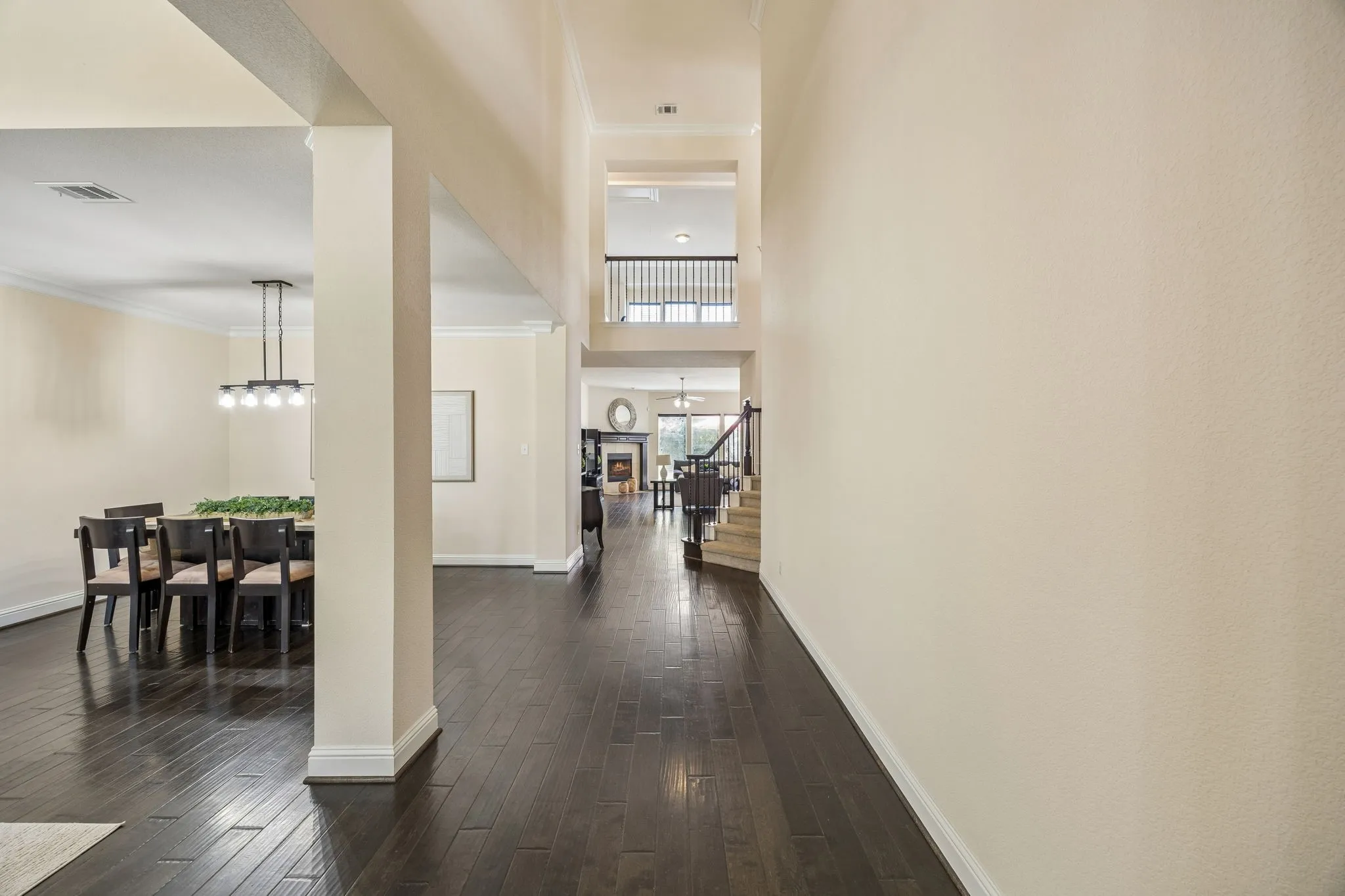 Rich wood-finish flooring throughout, two-story ceiling, open concept layout, modern chandelier, and dark wood staircase railing