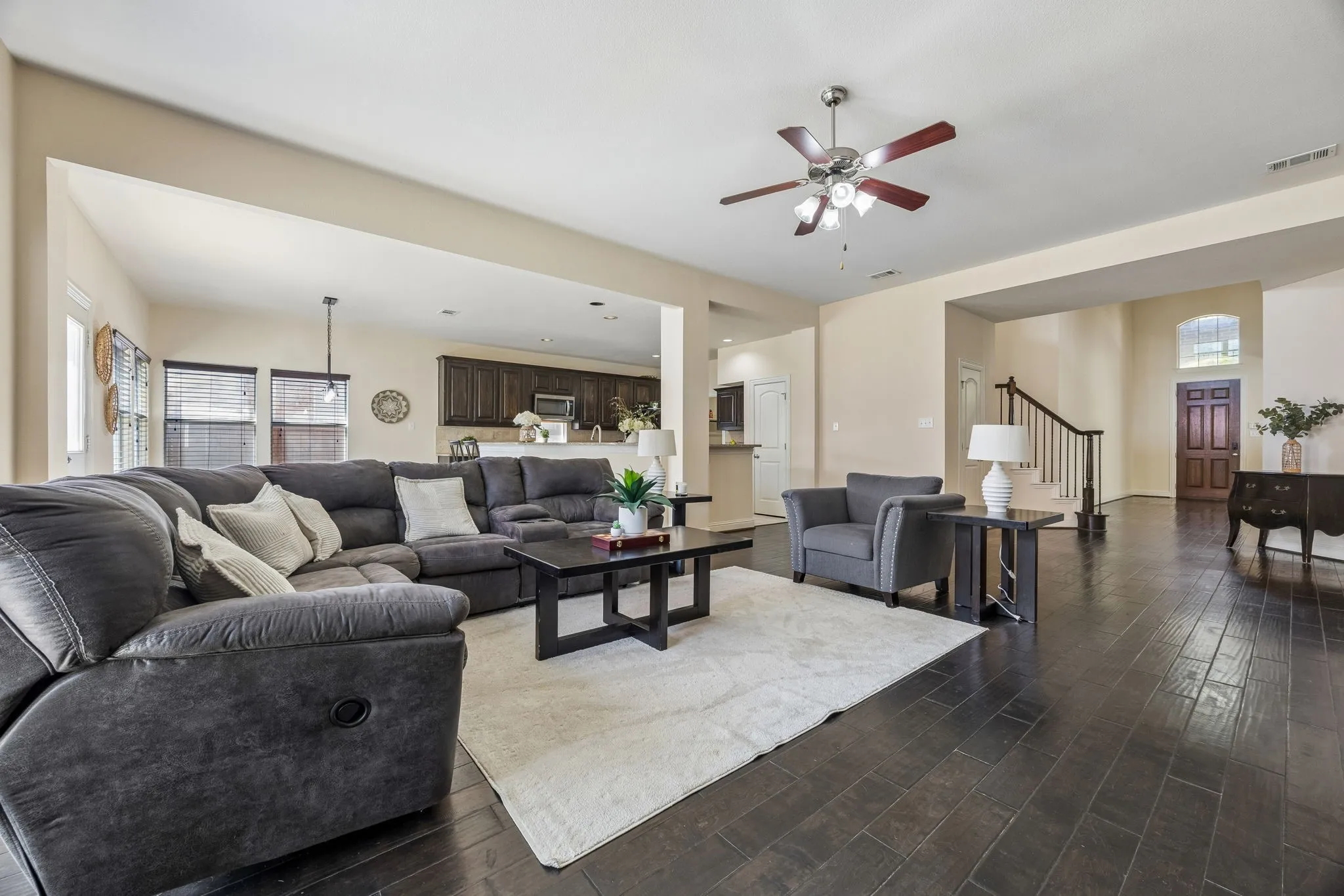 Dark wood-finish flooring throughout, ceiling fan with integrated lighting, built-in staircase with dark wood handrail, recessed wall archway, and wood panel front door