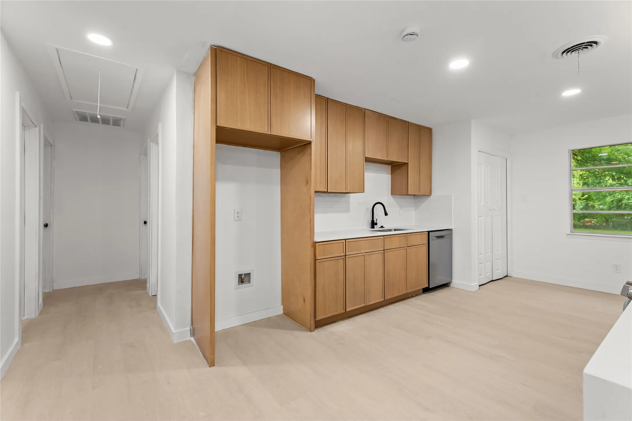 Light wood-finish flooring, recessed lighting, wood cabinetry, white countertops, and a stainless steel dishwasher