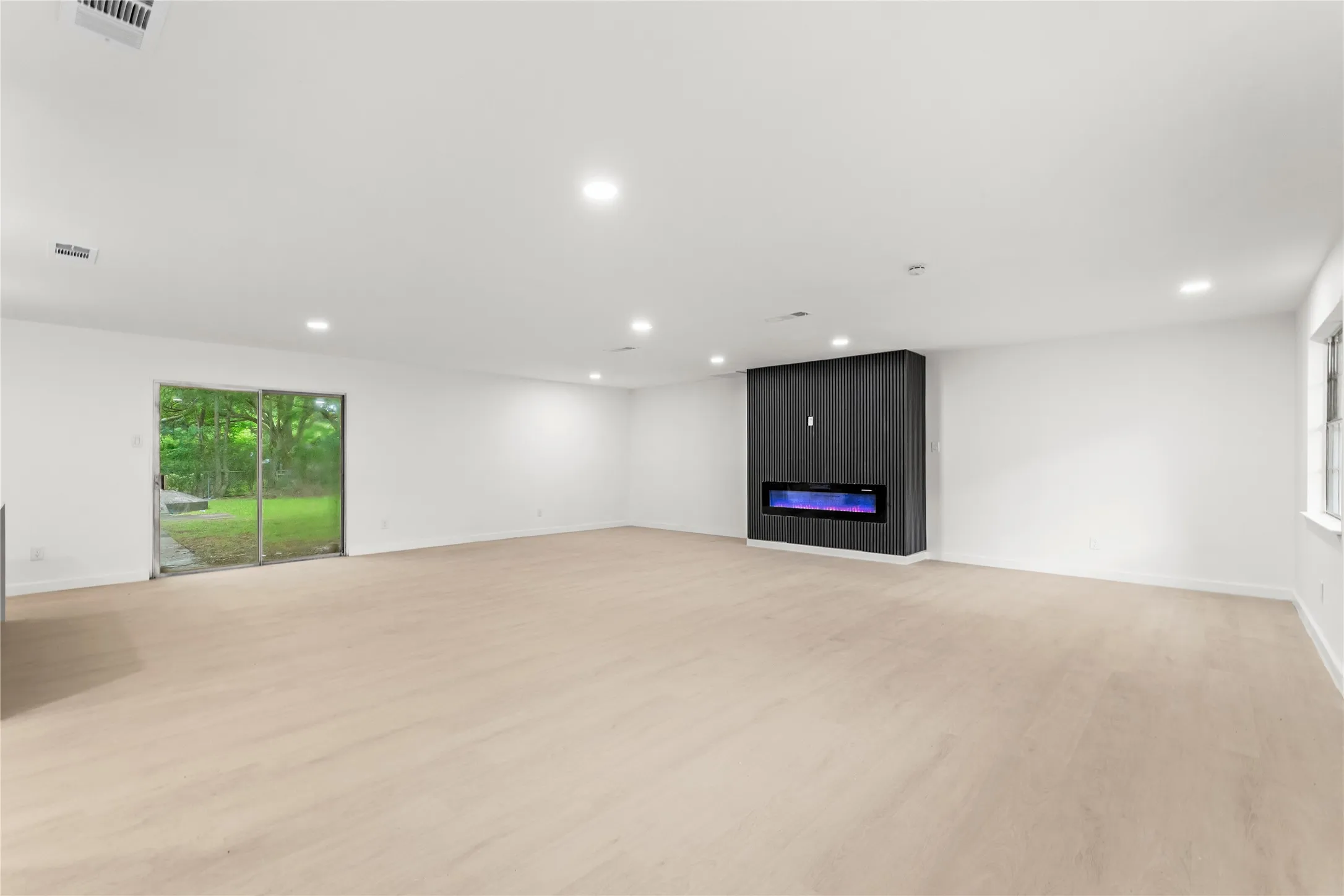 Spacious room with wood-finish flooring, recessed lighting, and a modern built-in fireplace feature