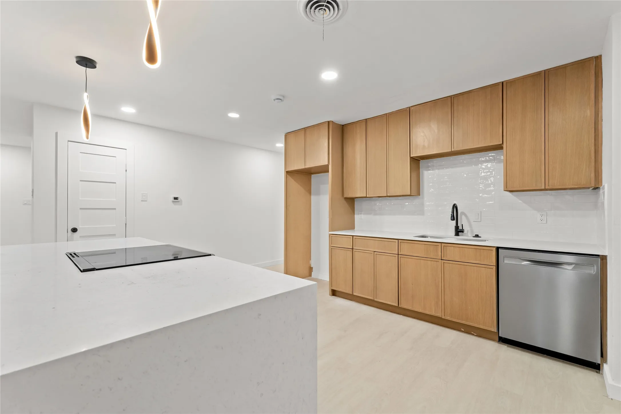 Modern kitchen featuring wood-finish cabinetry, quartz countertops, a tile backsplash, stainless steel dishwasher, and an integrated cooktop on the center island