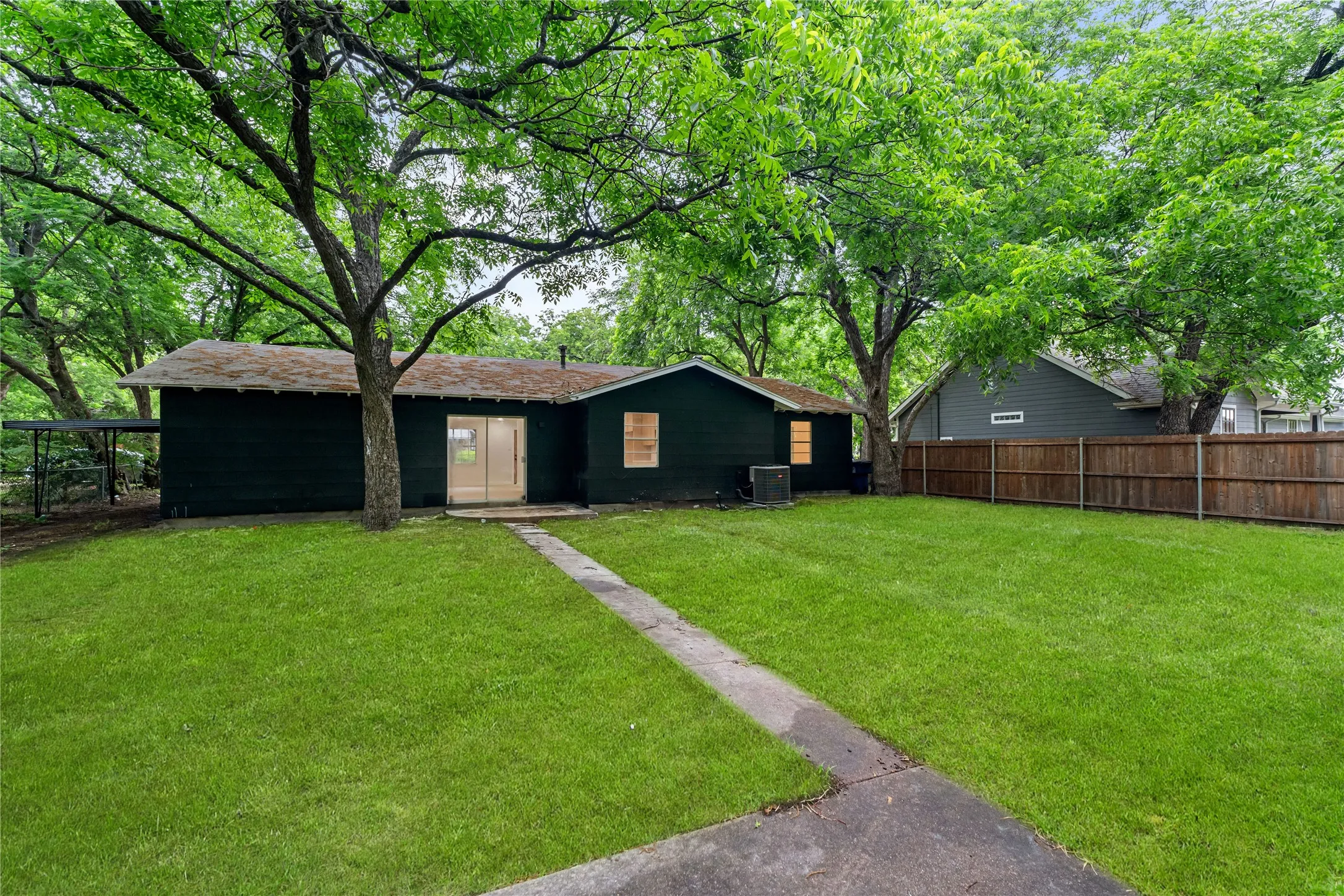 Expansive rear yard with a concrete pathway, mature trees, and a full privacy fence