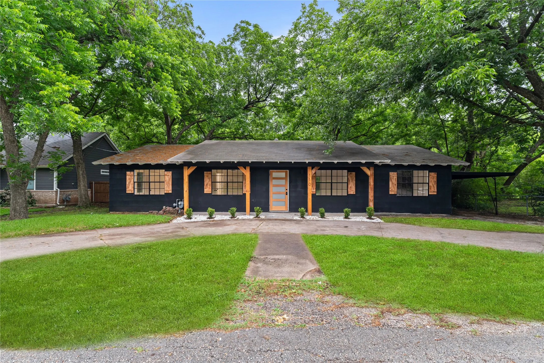 Ranch-style exterior with dark siding and wood accents, featuring a dual driveway and an attached carport