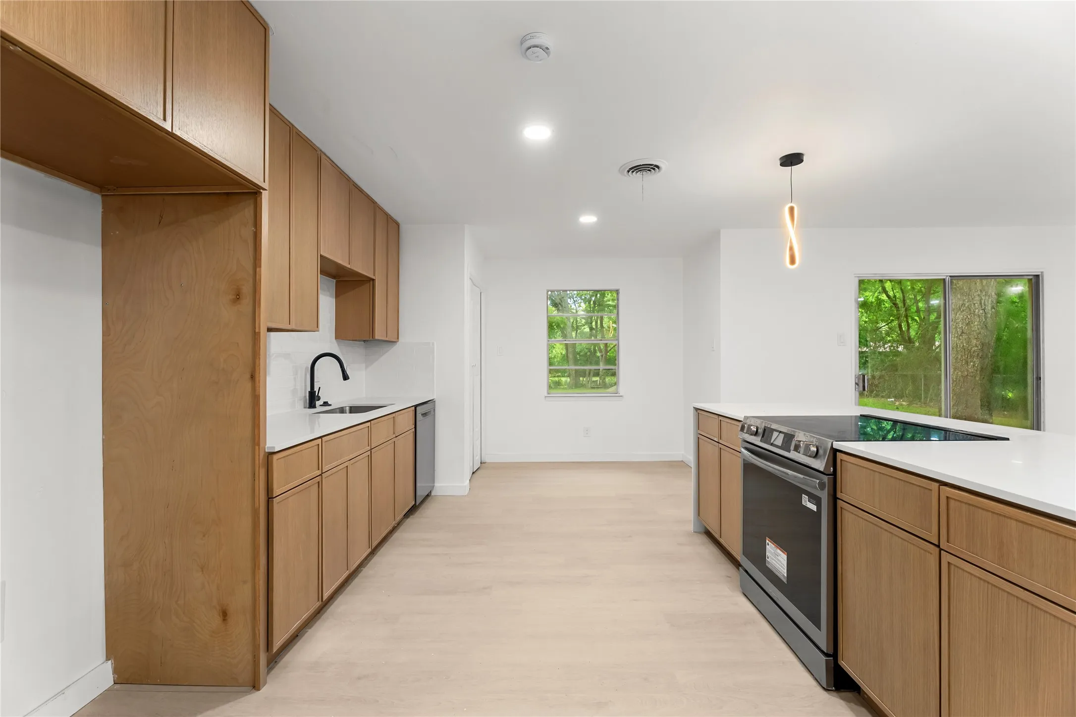 Modern kitchen featuring wood-finish cabinetry, light-toned wood-finish flooring, white countertops, stainless steel appliances, and a matte black faucet