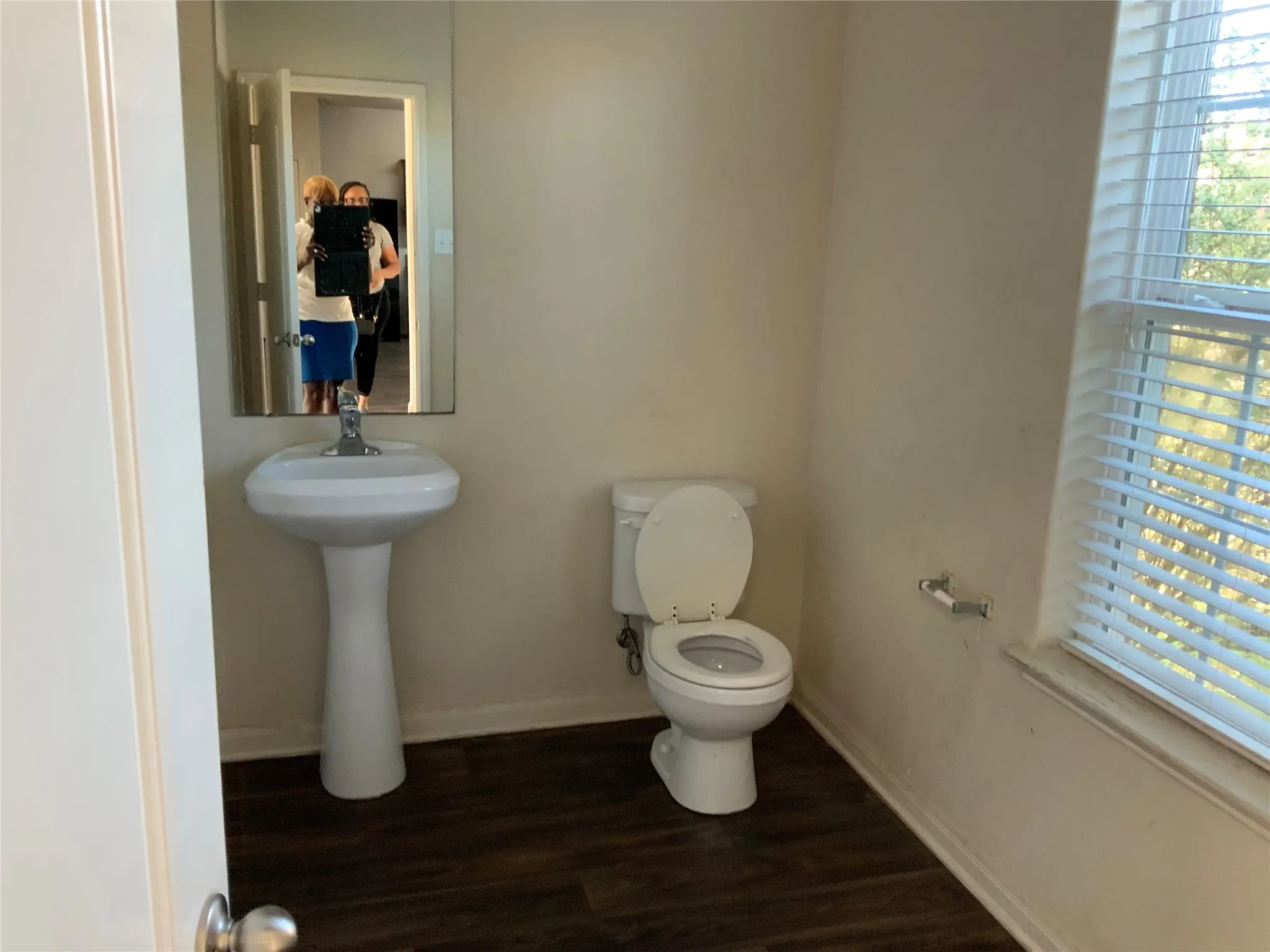 Pedestal sink with mirror, toilet, and wood-finish flooring