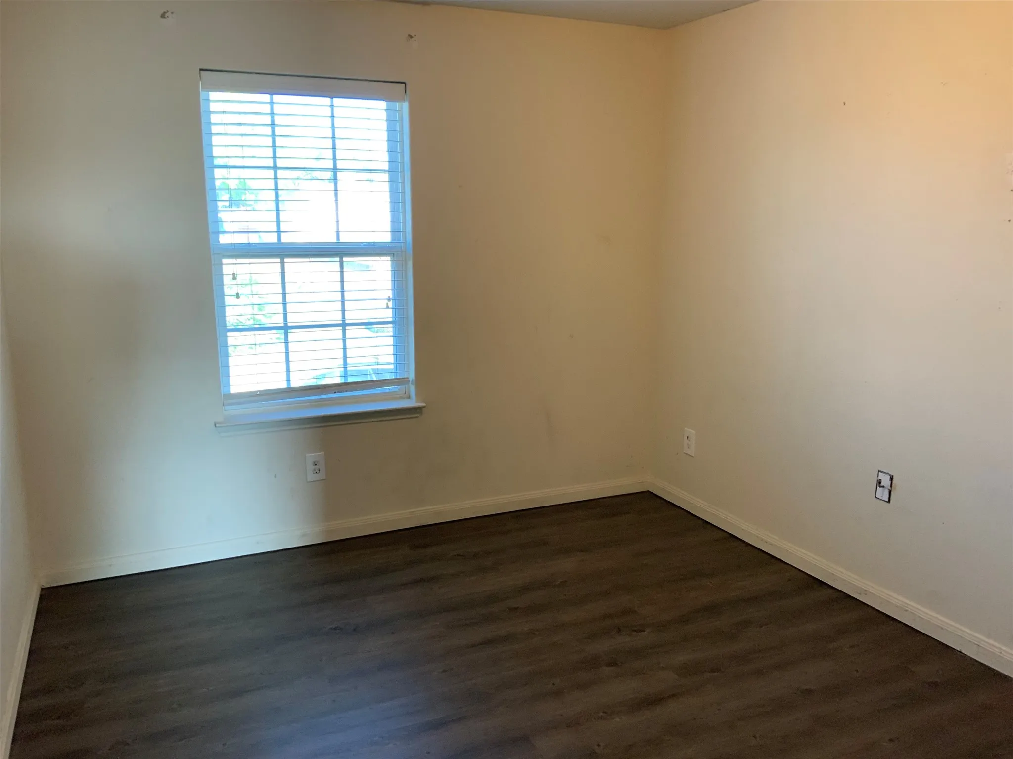 Wood-finish flooring with a window featuring horizontal blinds