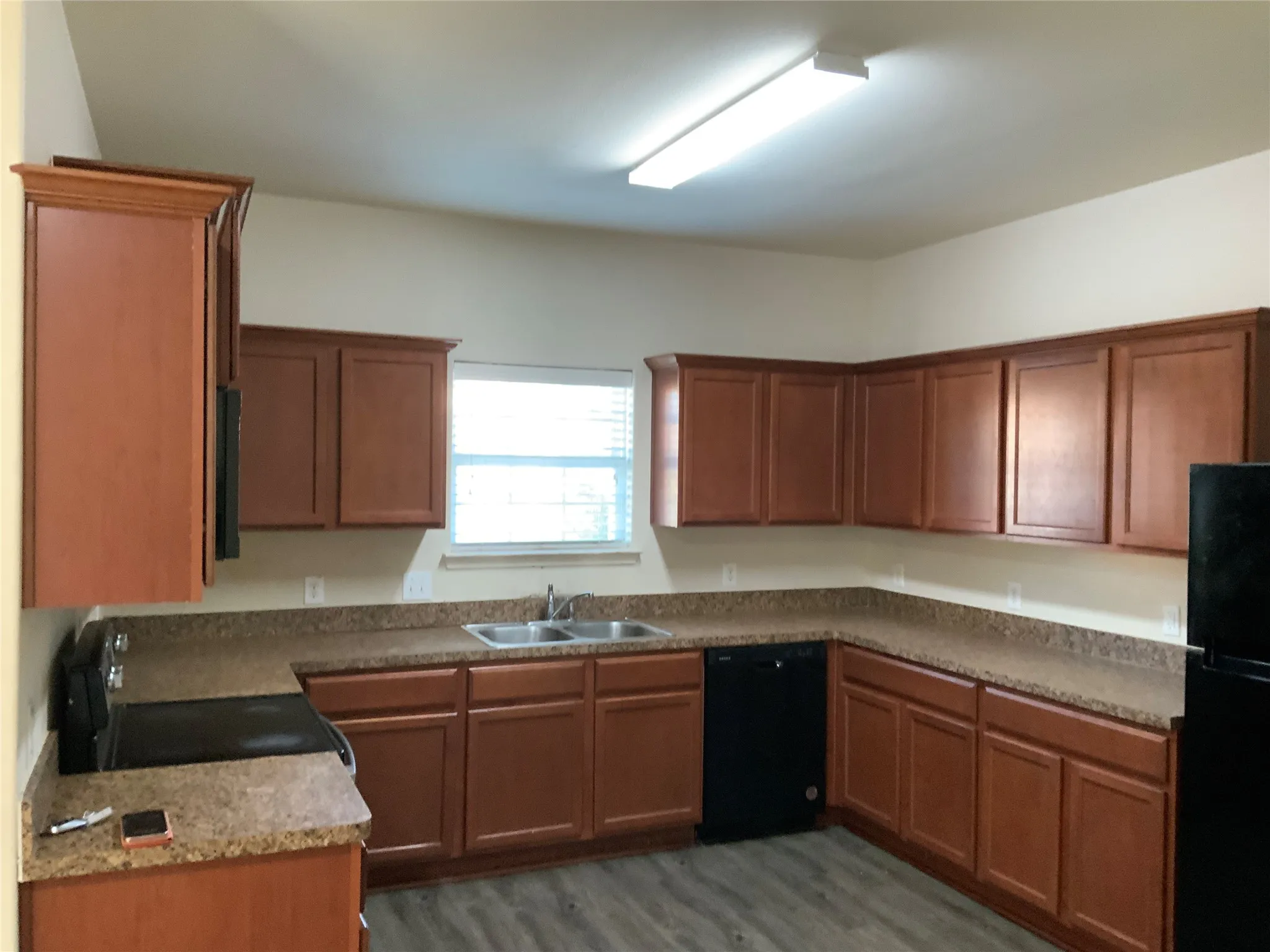 U-shaped kitchen featuring wood-finish cabinetry, speckled countertops, stainless steel double basin sink, black built-in dishwasher, and wood-finish flooring