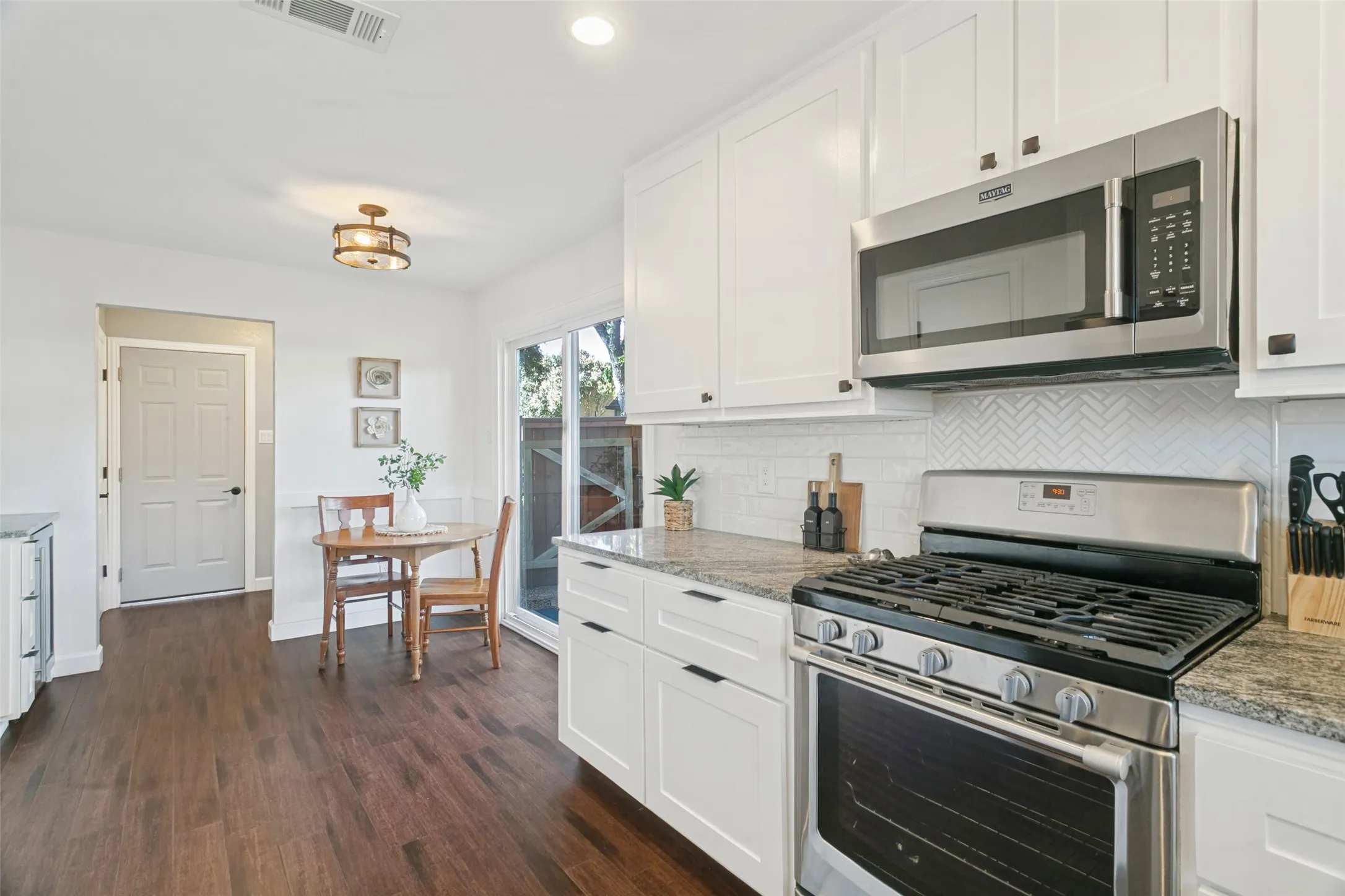 Wood floors carry throughout the kitchen with an eat-in dining area, decorative lighting and a sliding glass door leading to the side backyard.