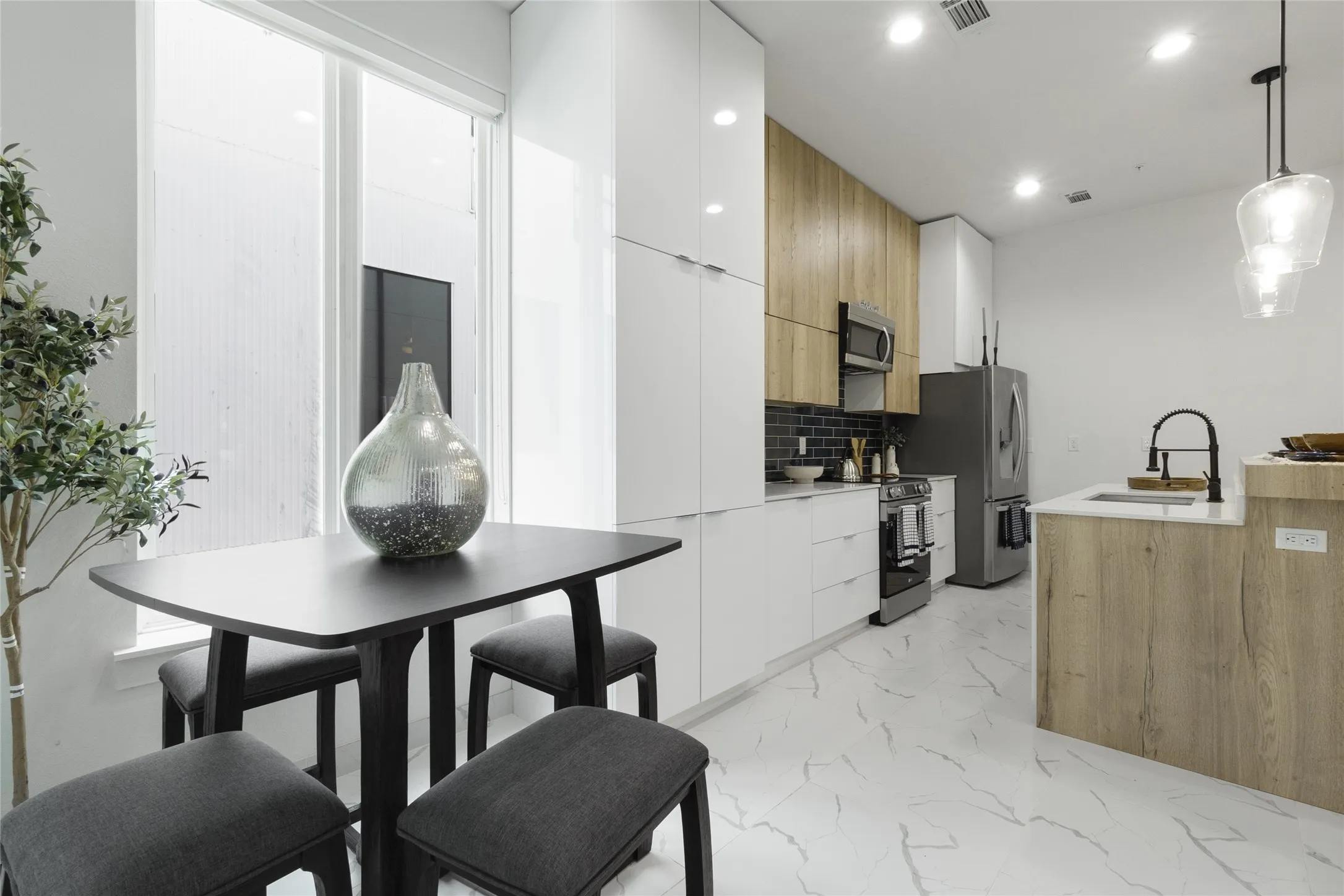Modern kitchen featuring white and wood-finish cabinetry, stainless steel appliances, a dark subway tile backsplash, and an island with a white countertop