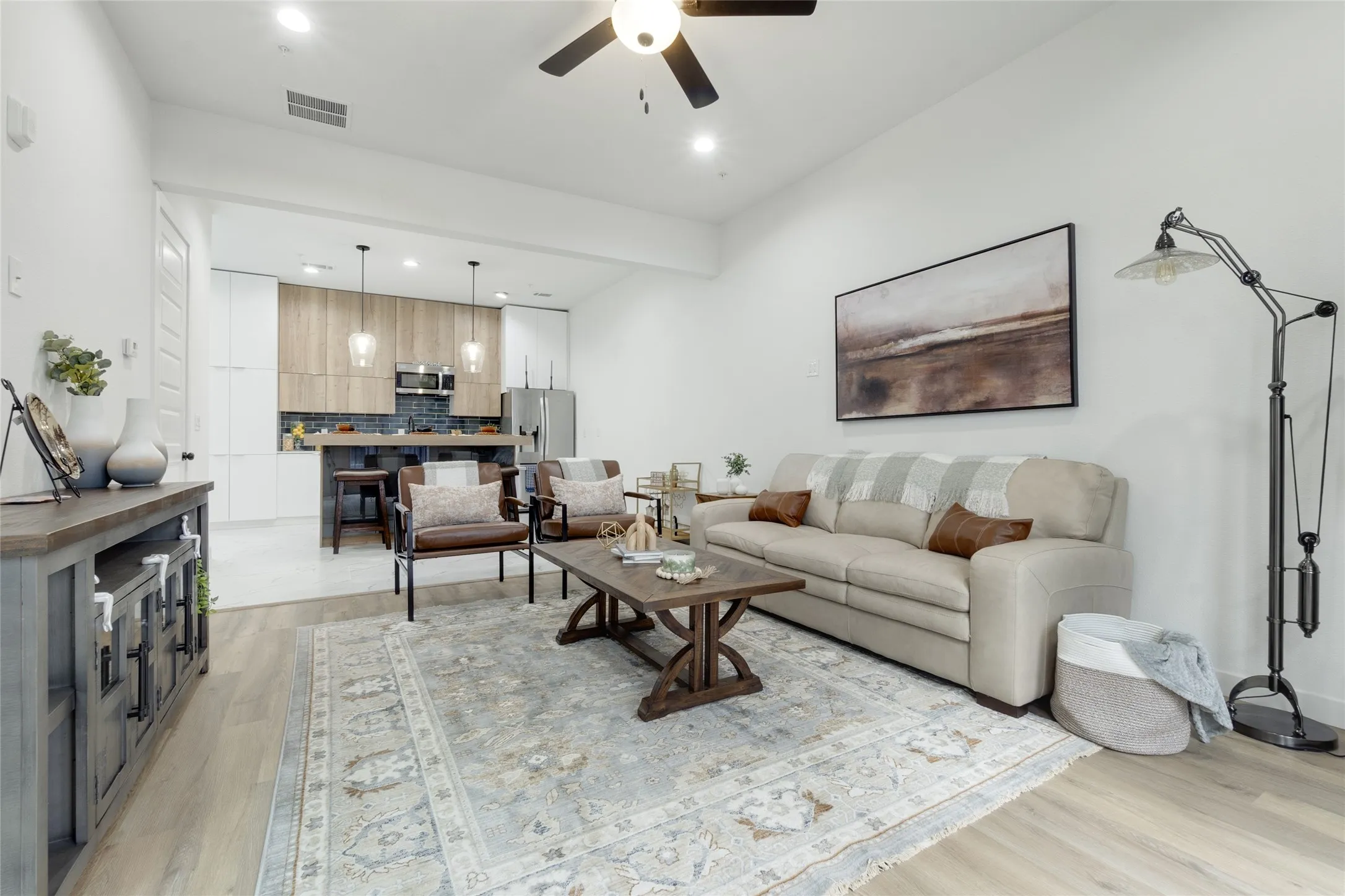 Open-concept living area featuring light wood-finish flooring, recessed lighting, a ceiling fan, and a kitchen with an island and pendant lighting