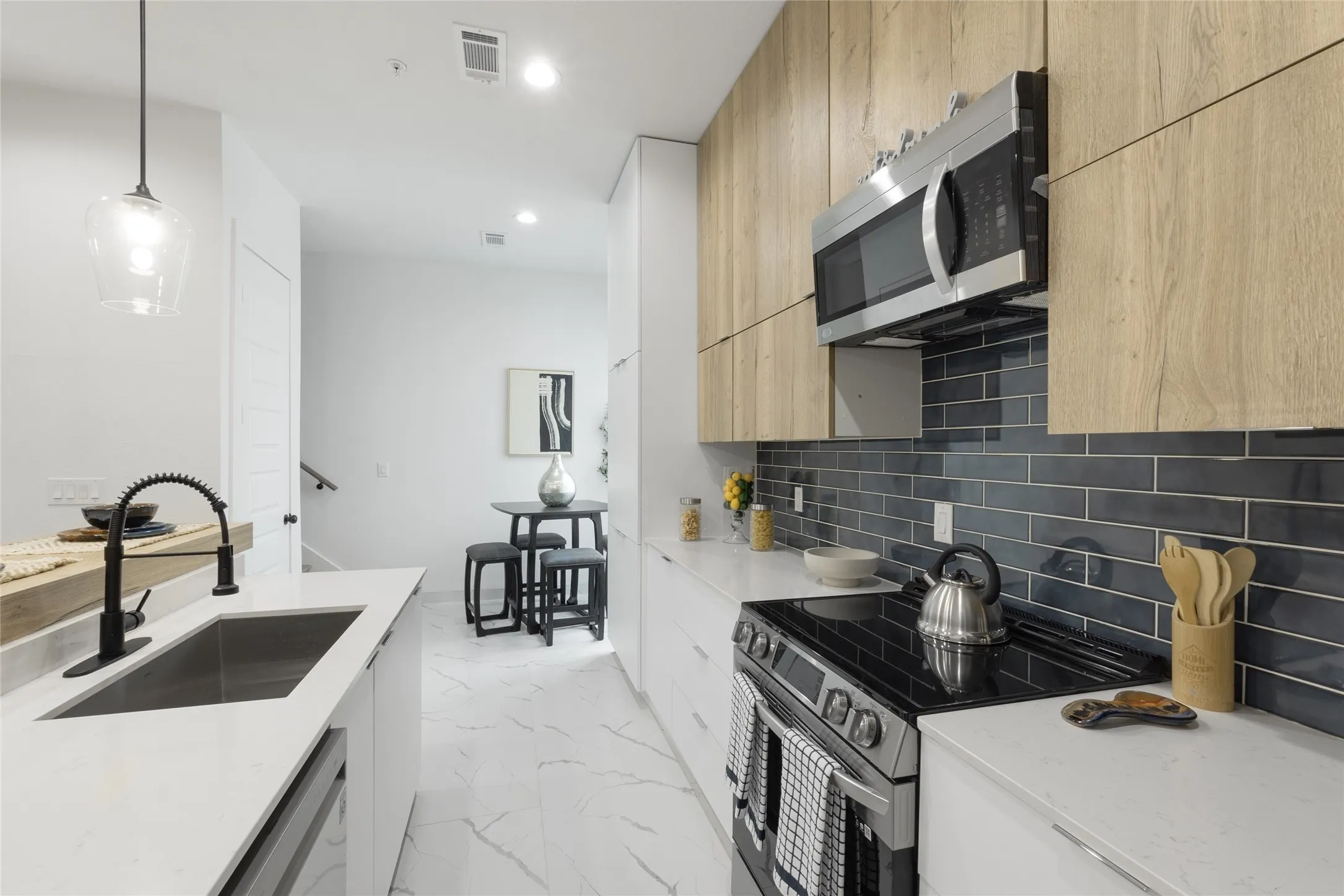 Modern kitchen featuring white countertops, stainless steel appliances, dark subway tile backsplash, and wood-finish cabinetry