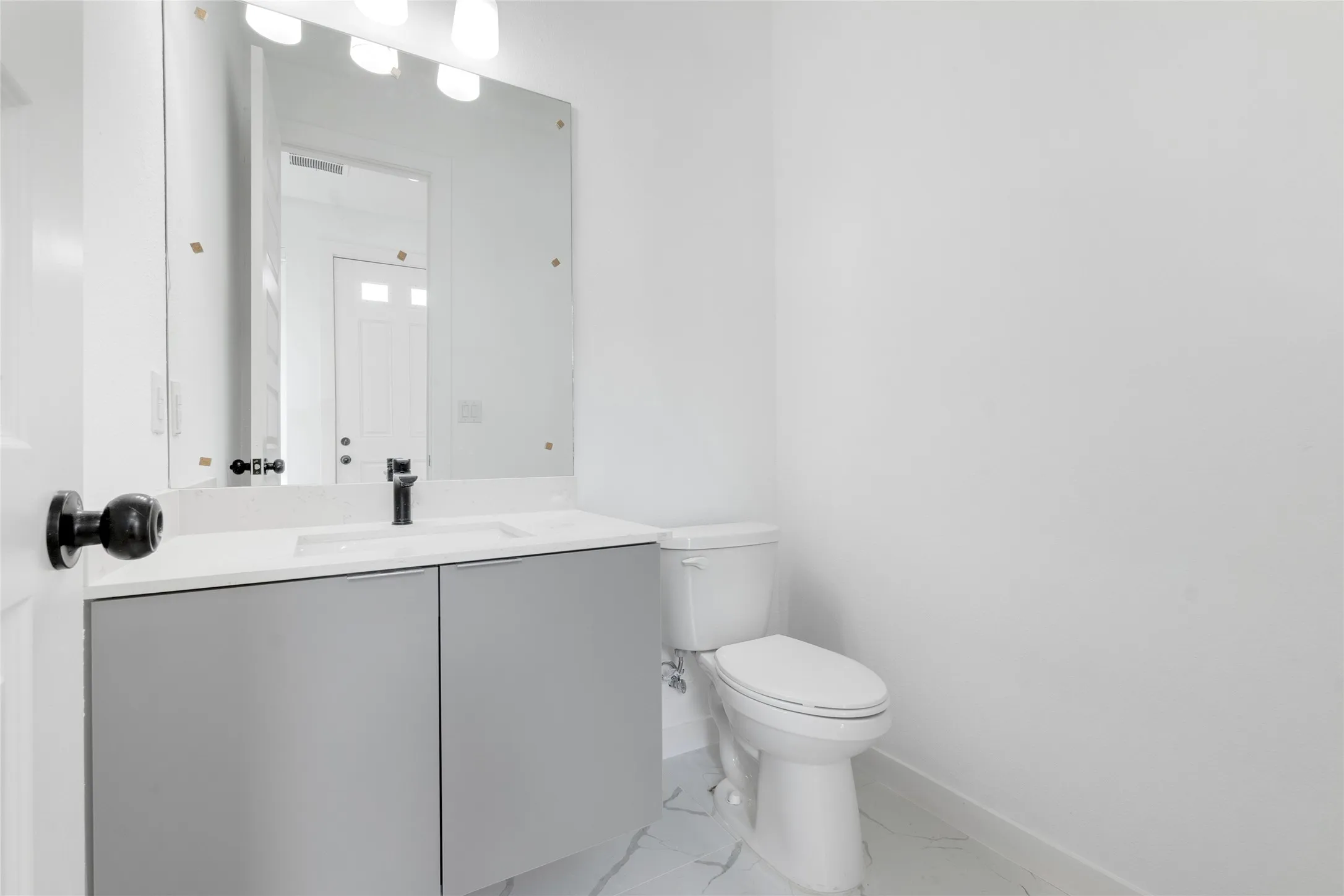 White walls, vanity with gray cabinetry, white countertop, black faucet, and white toilet