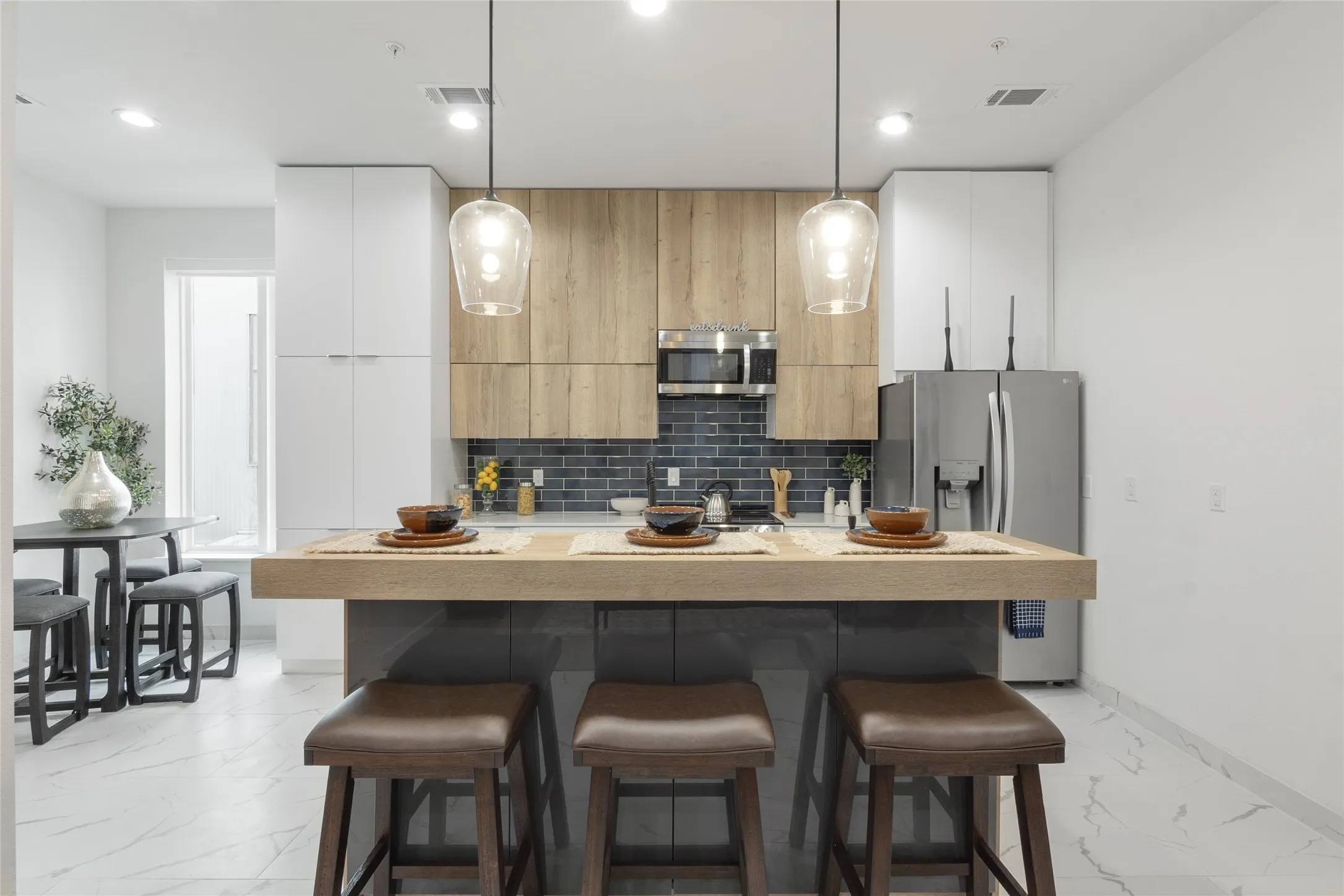 Kitchen featuring stainless steel appliances, wood-finish cabinetry, a dark tile backsplash, and a central island with pendant lighting