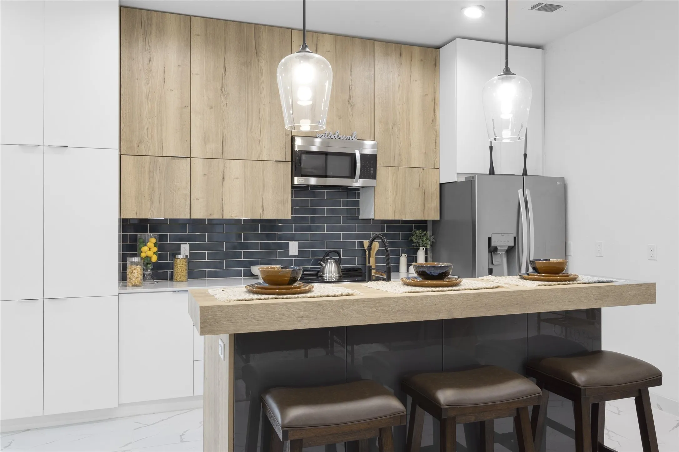 Contemporary kitchen featuring wood-finish cabinetry, white flat-panel cabinetry, a dark subway tile backsplash, stainless steel appliances, and a kitchen island with seating