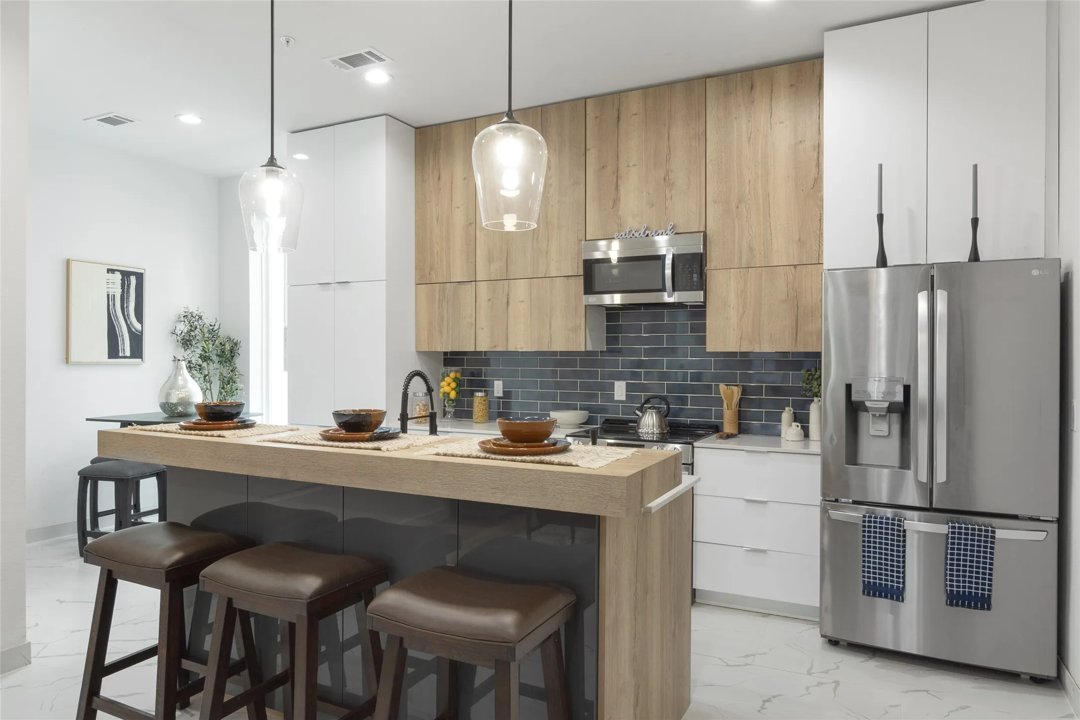 Kitchen featuring a central island with counter seating, stainless steel appliances, white and wood-finish cabinetry, and a subway tile backsplash