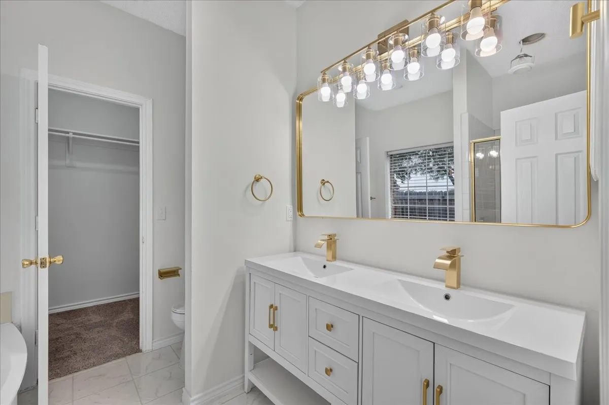 Dual vanity with integrated sinks, gold-finish hardware, and a large framed mirror