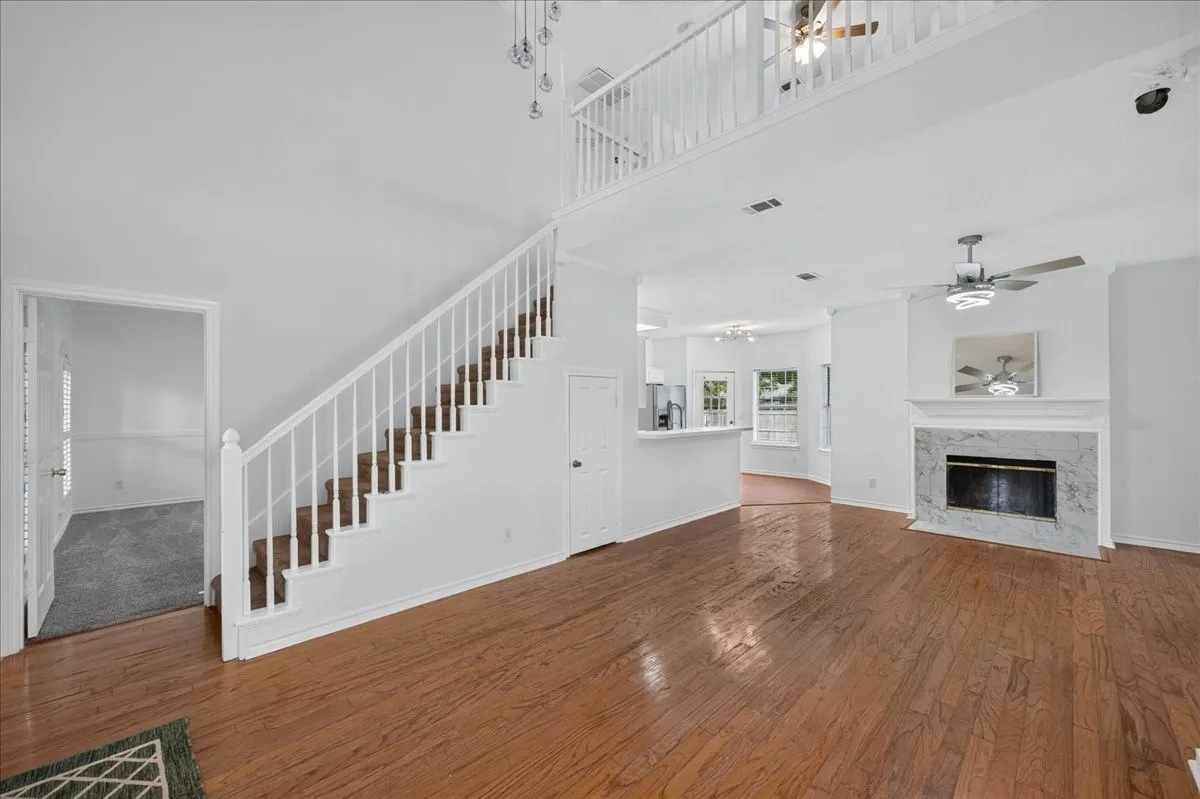 Hardwood flooring throughout, a white baluster staircase, a marble-surround fireplace, a lofted area with white railings, and a breakfast bar