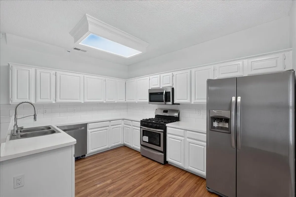 Kitchen featuring white cabinetry, subway tile backsplash, wood-finish flooring, stainless steel appliances, and a recessed ceiling light fixture