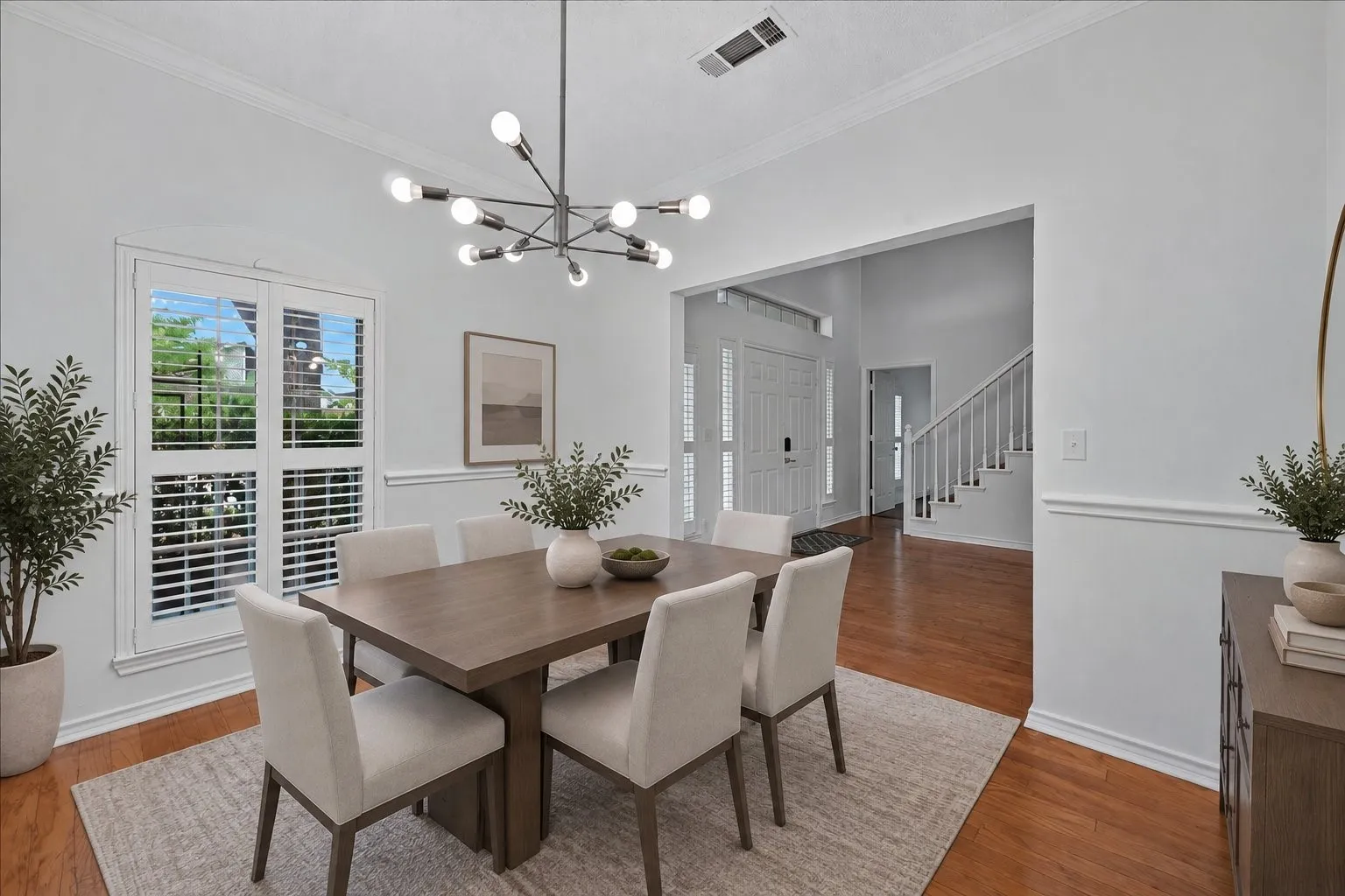 Hardwood flooring throughout, crown molding, modern sputnik chandelier, white plantation shutters, and a prominent staircase with white balusters