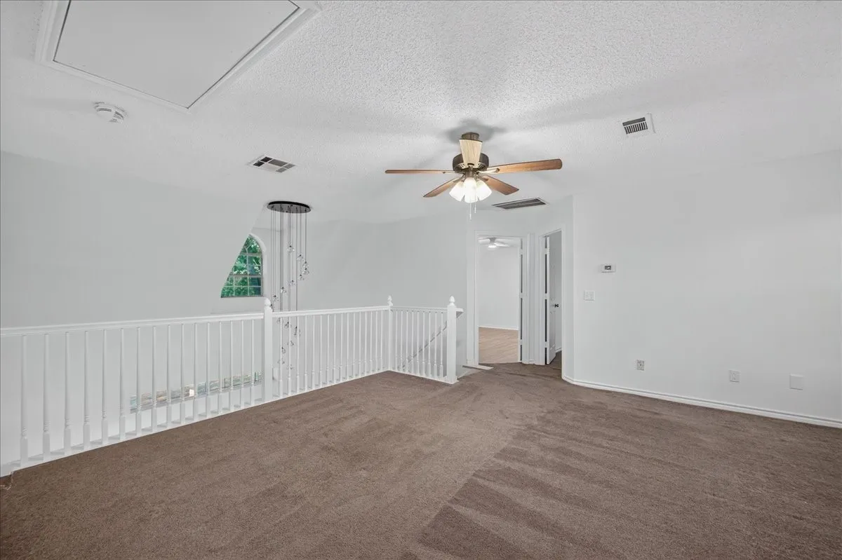 Carpeted loft area with a ceiling fan, white railings, and a distinct arched window