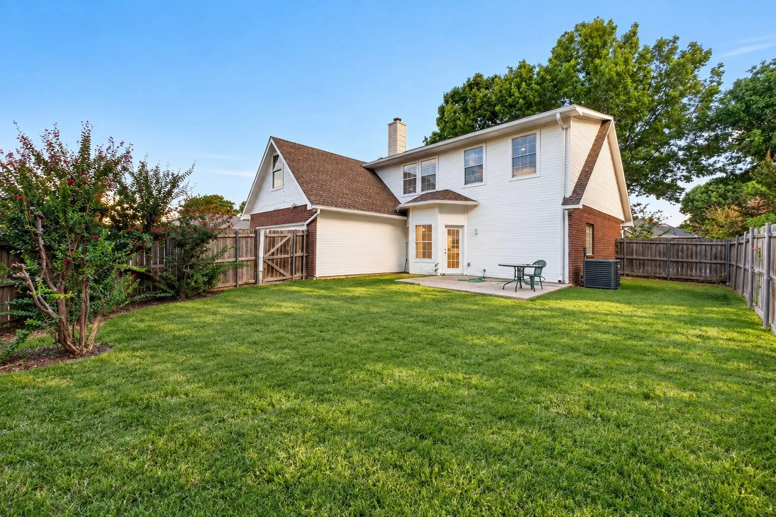 Expansive backyard featuring a lush lawn, privacy fencing, a concrete patio, and mature landscaping