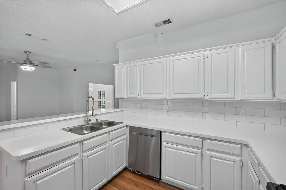 Kitchen featuring white cabinetry, light-toned countertops, a stainless steel double sink, a subway tile backsplash, and wood-finish flooring