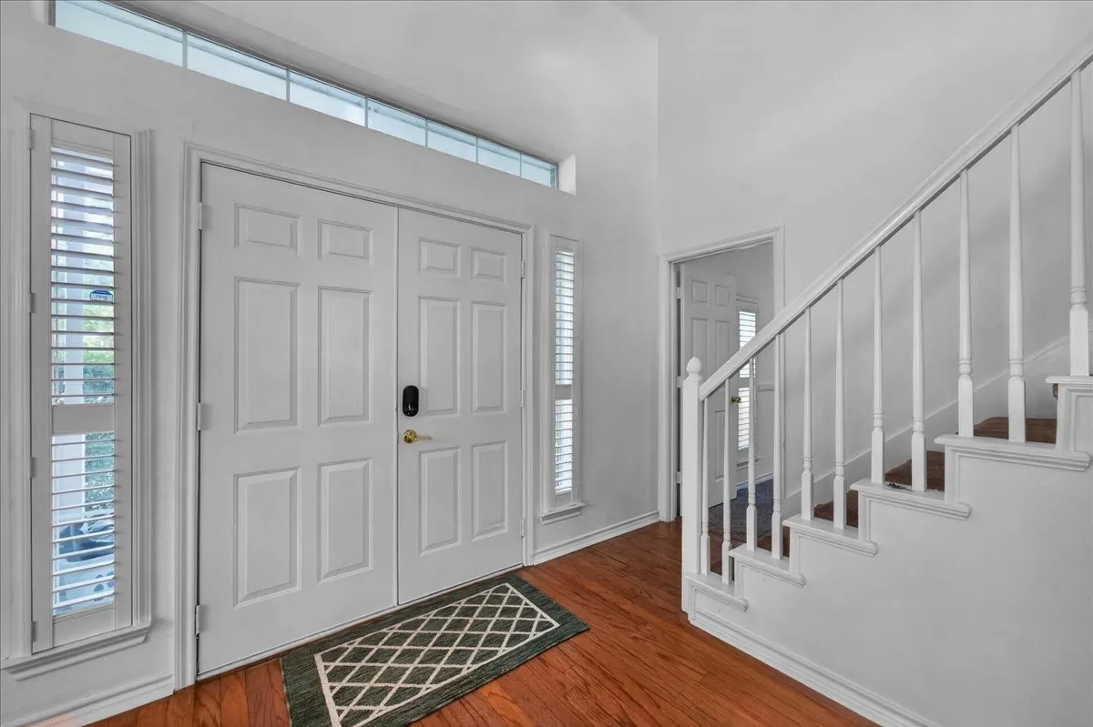 Double entry doors with transom window, plantation shutters, wood-finish flooring, and a white staircase with balusters