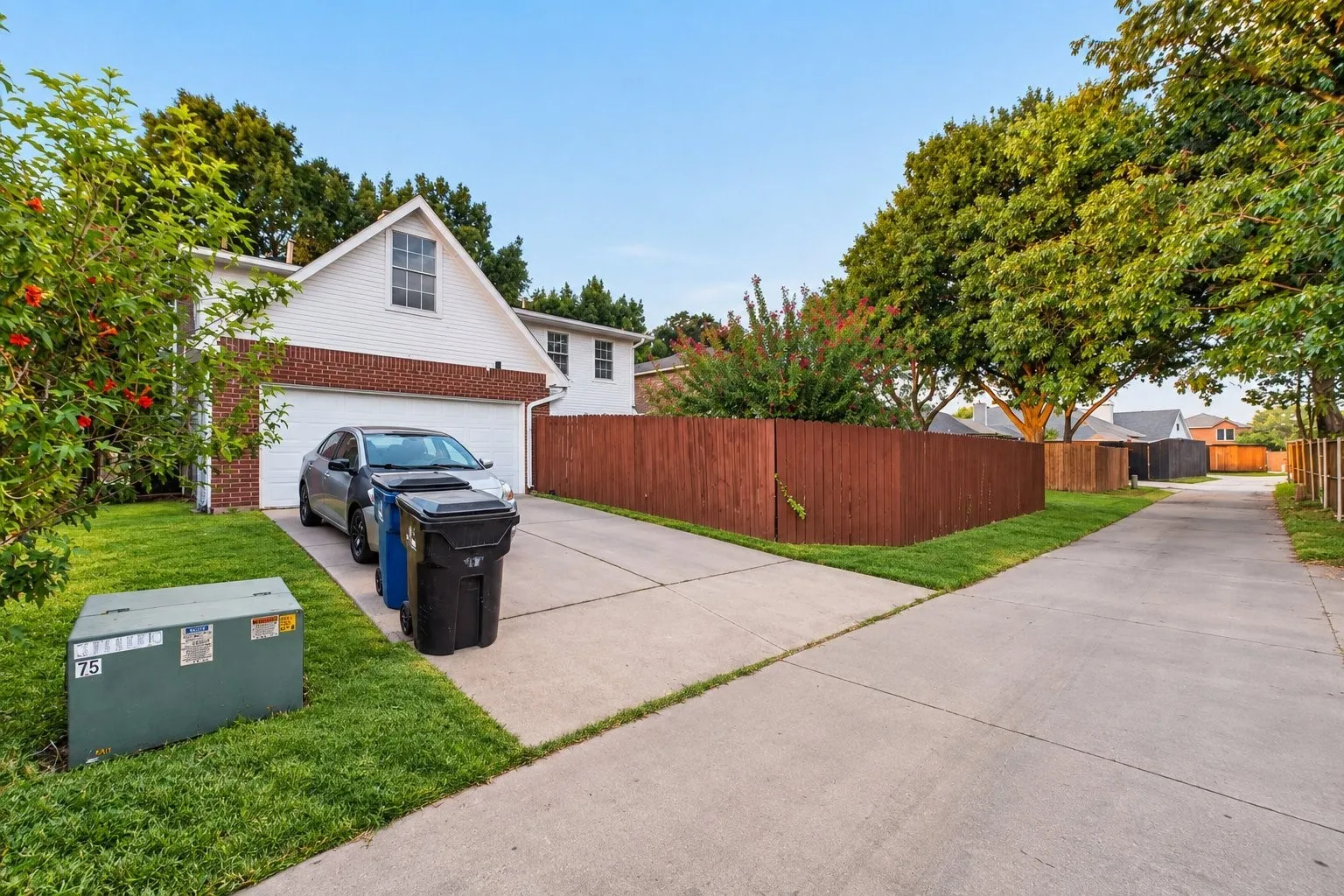 White siding with a brick facade accent, attached garage, concrete driveway, and a well-maintained lawn