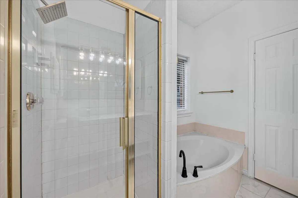 Glass-enclosed shower with a brushed nickel showerhead, corner soaking tub with matte black fixtures, and white tile flooring