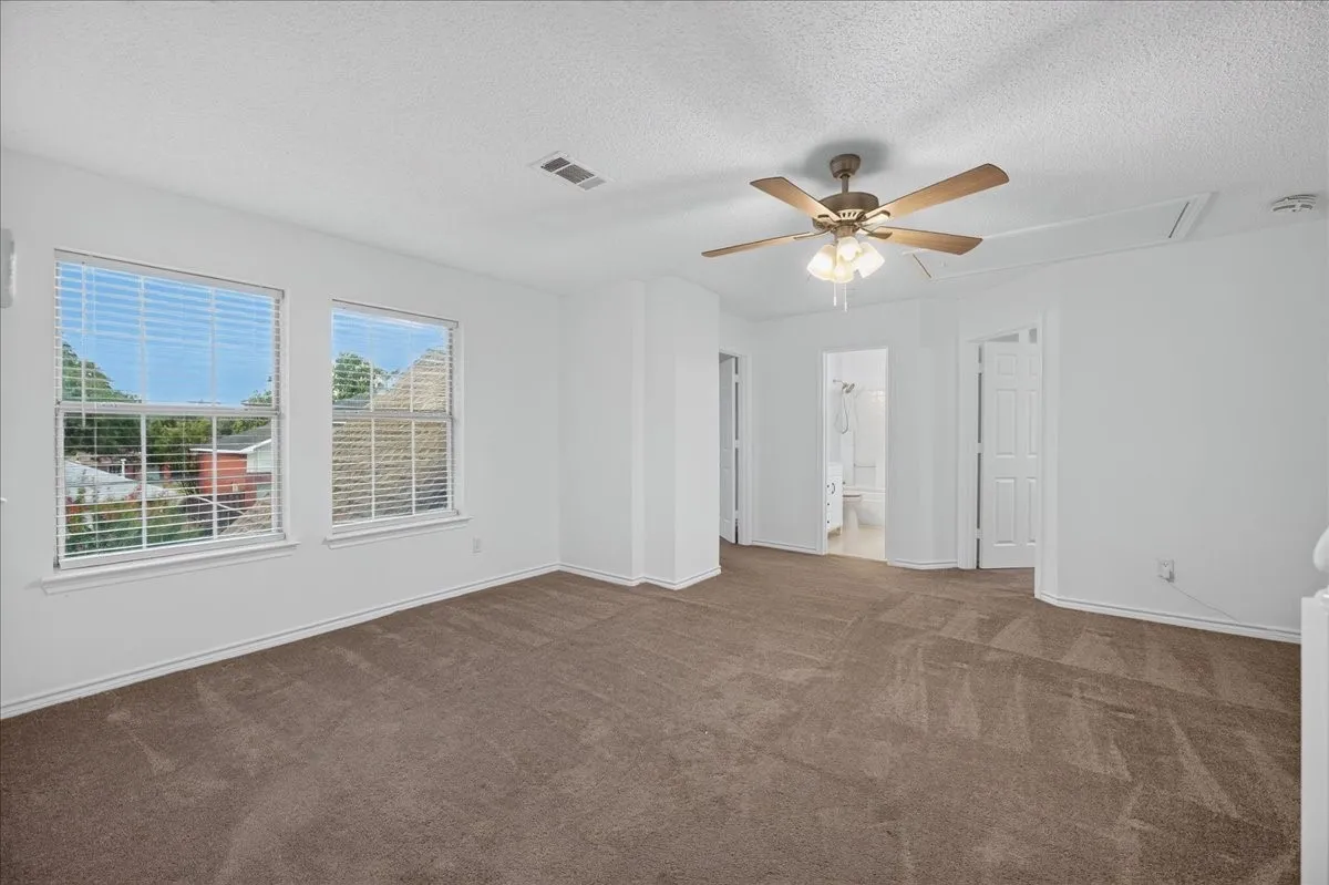 Spacious room with carpet flooring, two windows, and a ceiling fan