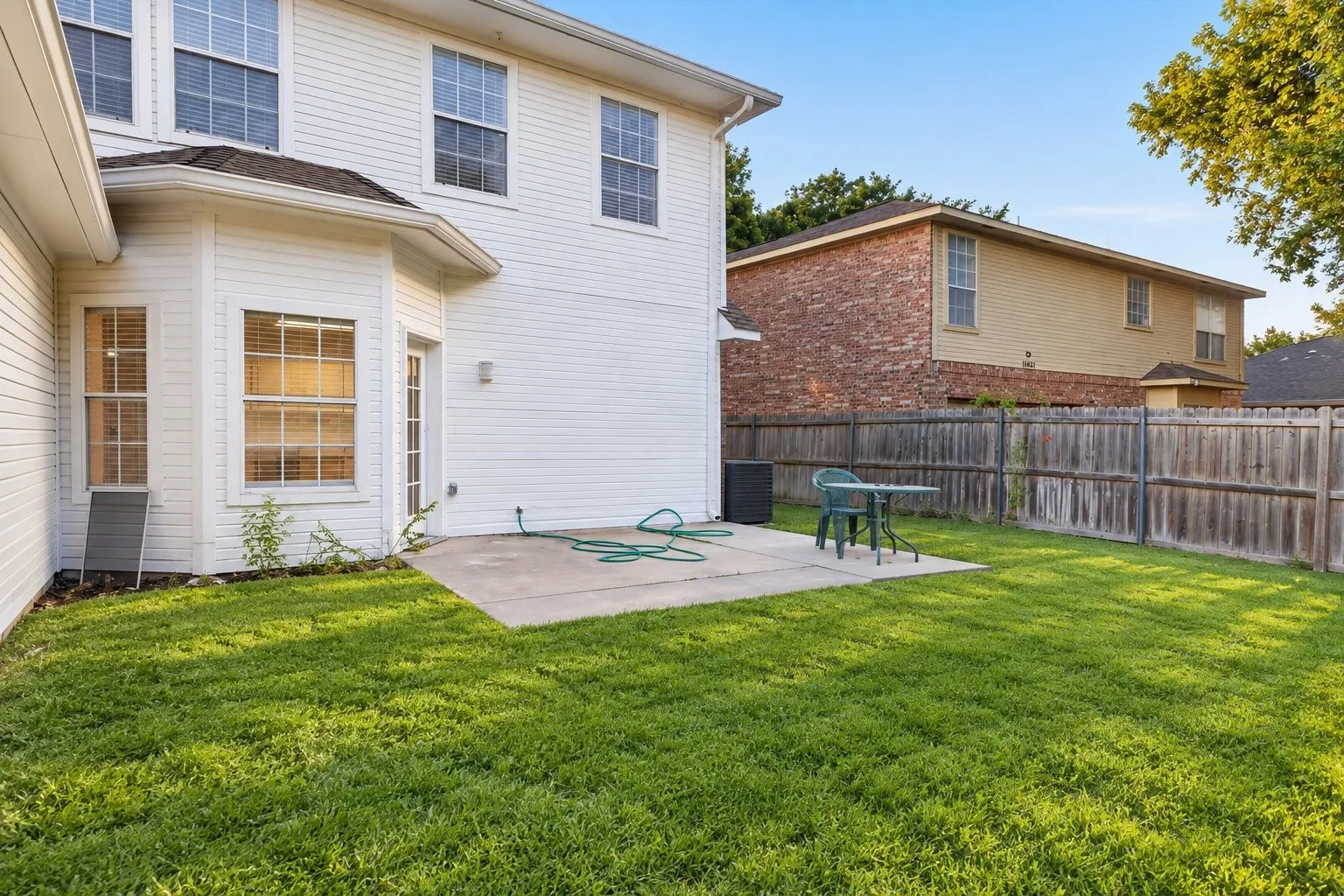 Expansive grassy area with a concrete patio, wood privacy fencing, and multiple windows