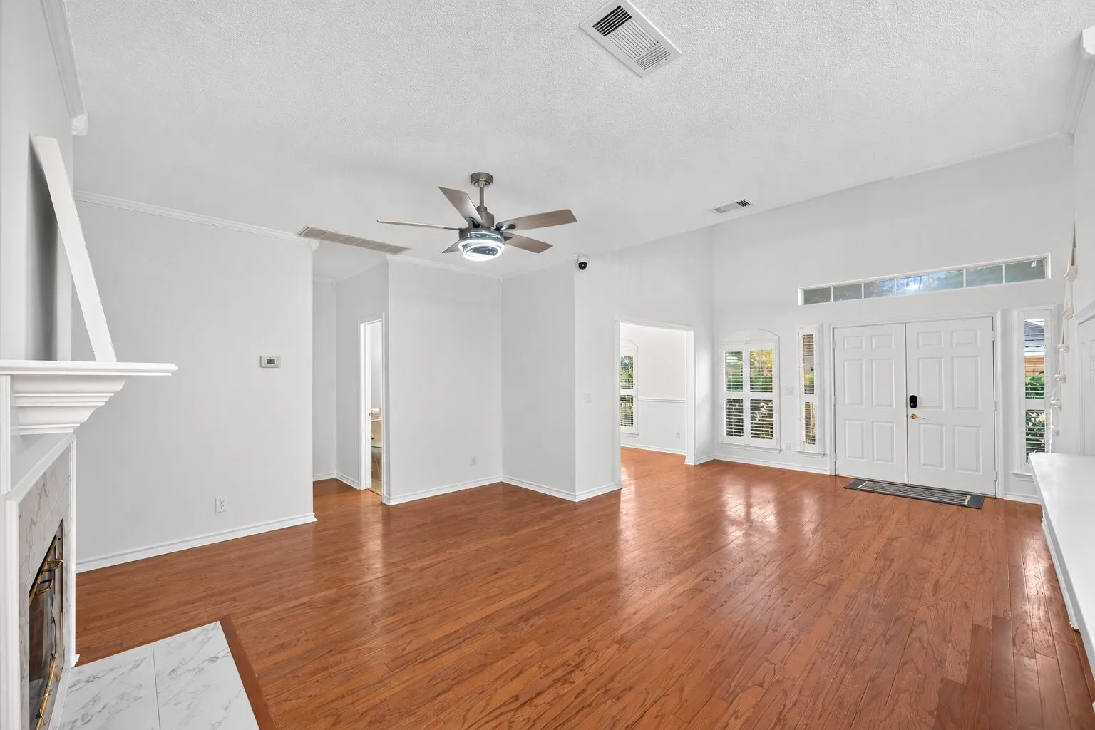 Vaulted ceiling, wood-finish flooring, white double front doors, transom window, and a fireplace with a white mantel and marble surround