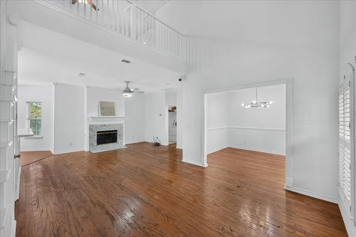 Spacious living area featuring wood-finish flooring, a fireplace with a stone surround and mantel, and an open-concept dining area with a contemporary chandelier
