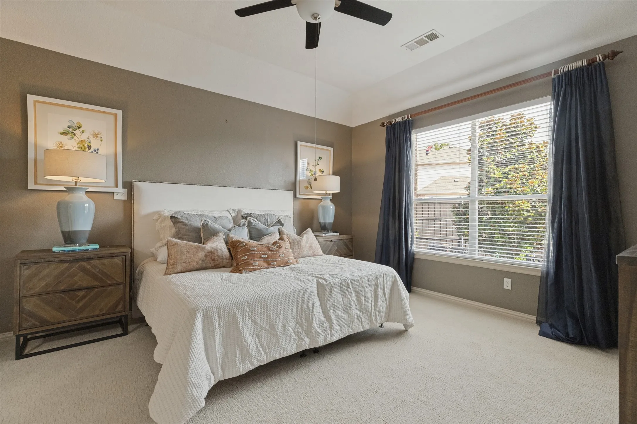 Spacious primary bedroom featuring brand-new carpet, a tray ceiling, ceiling fan, and large window that fills the room with natural light, creating a comfortable and relaxing retreat.