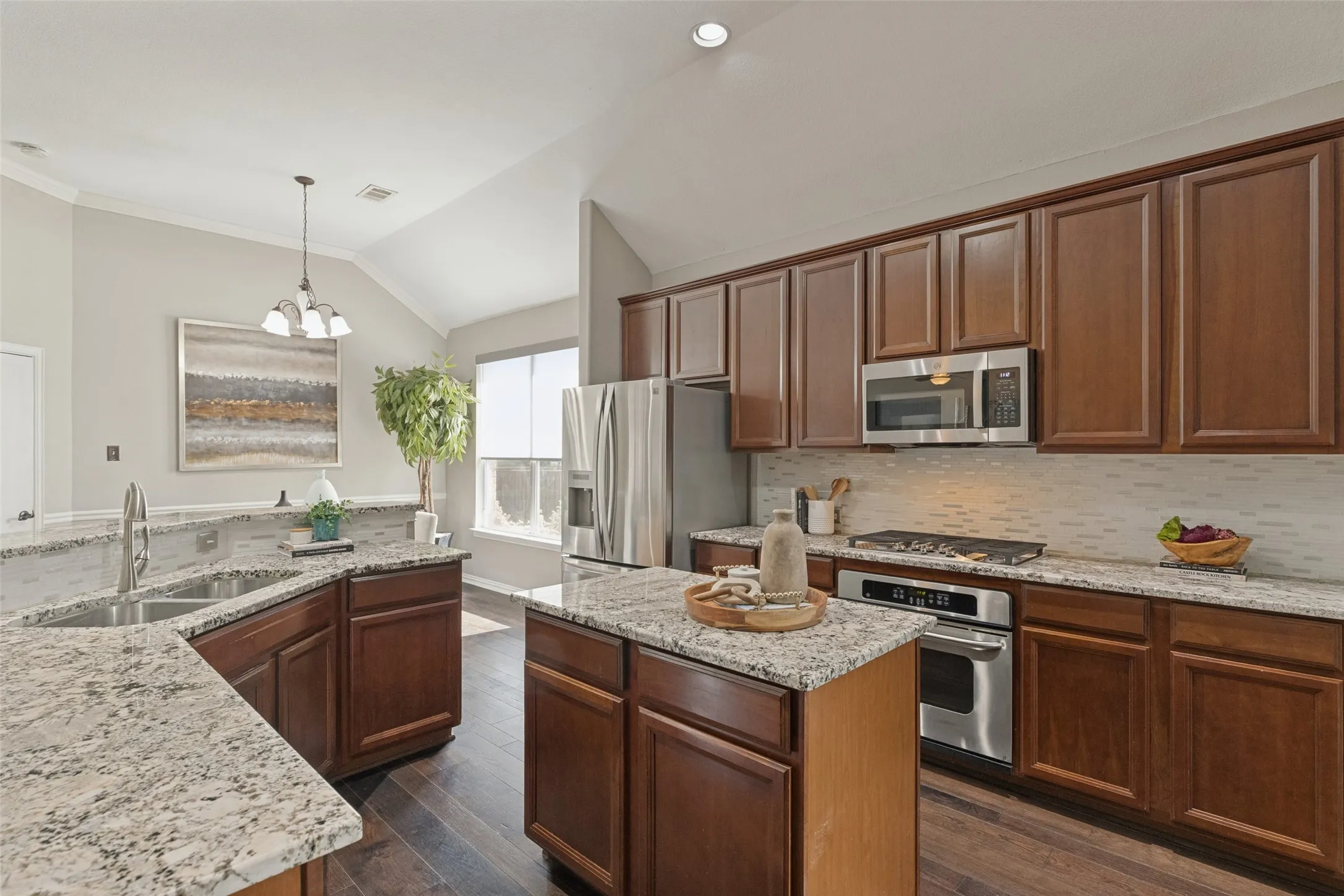 Well-appointed kitchen featuring granite countertops, rich wood cabinetry, stainless steel appliances, a gas cooktop, center island, and plenty of workspace, with a bright breakfast area just beyond.