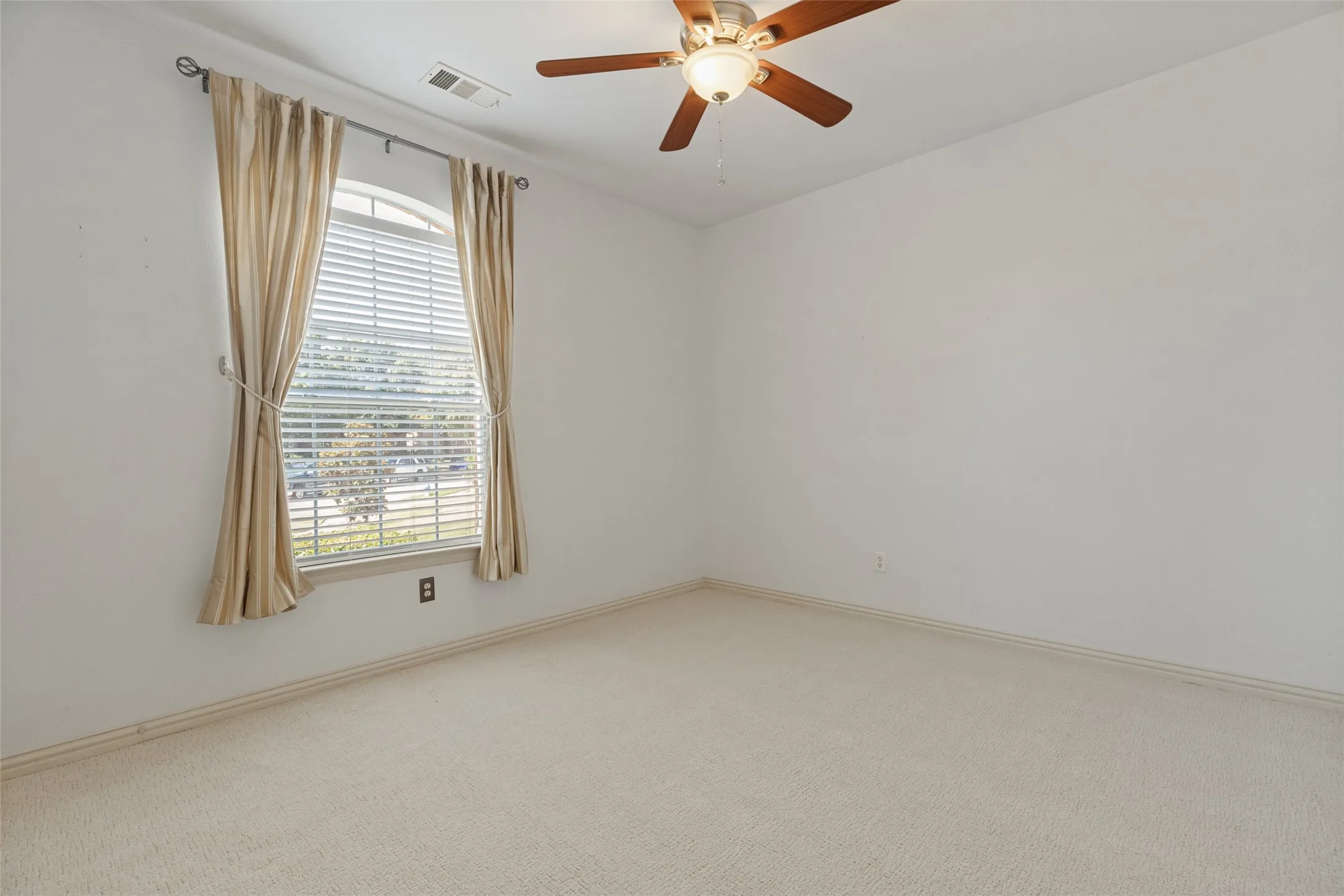 Spacious secondary bedroom featuring brand-new carpet, a ceiling fan, and a large arched window that brings in abundant natural light.