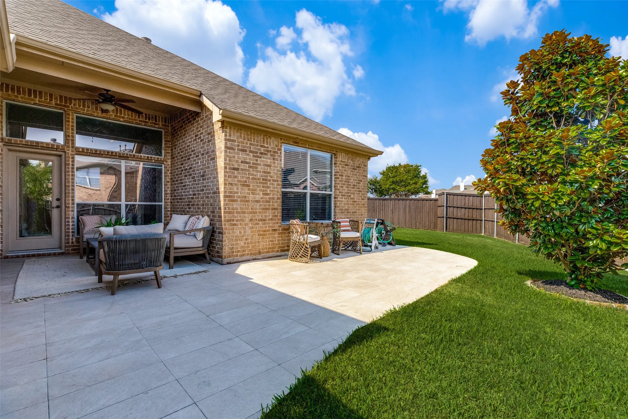 Spacious backyard features an extended patio with a covered seating area and ceiling fan, plus a beautifully maintained lawn with plenty of room to relax, entertain, and enjoy the outdoors.