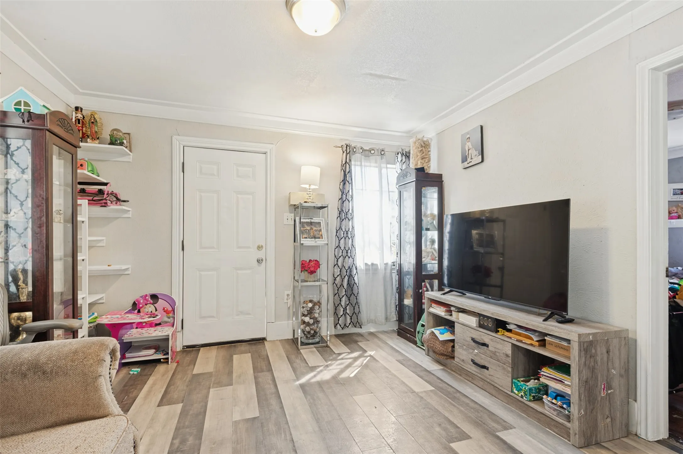 Wood-finish flooring, white paneled interior door, crown molding, and recessed ceiling light
