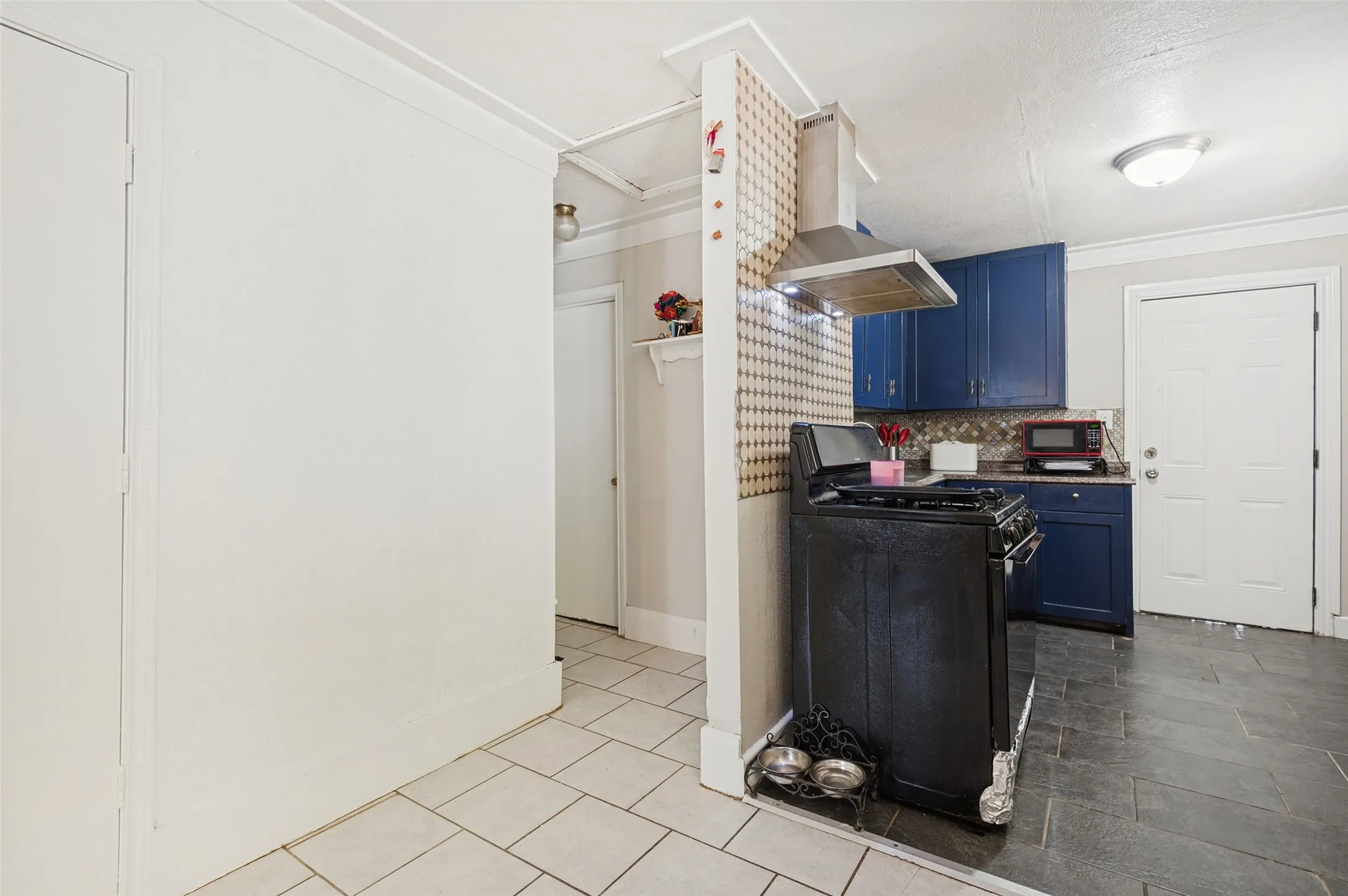 Kitchen area with dark blue cabinetry, a stainless steel range hood, and tile backsplash