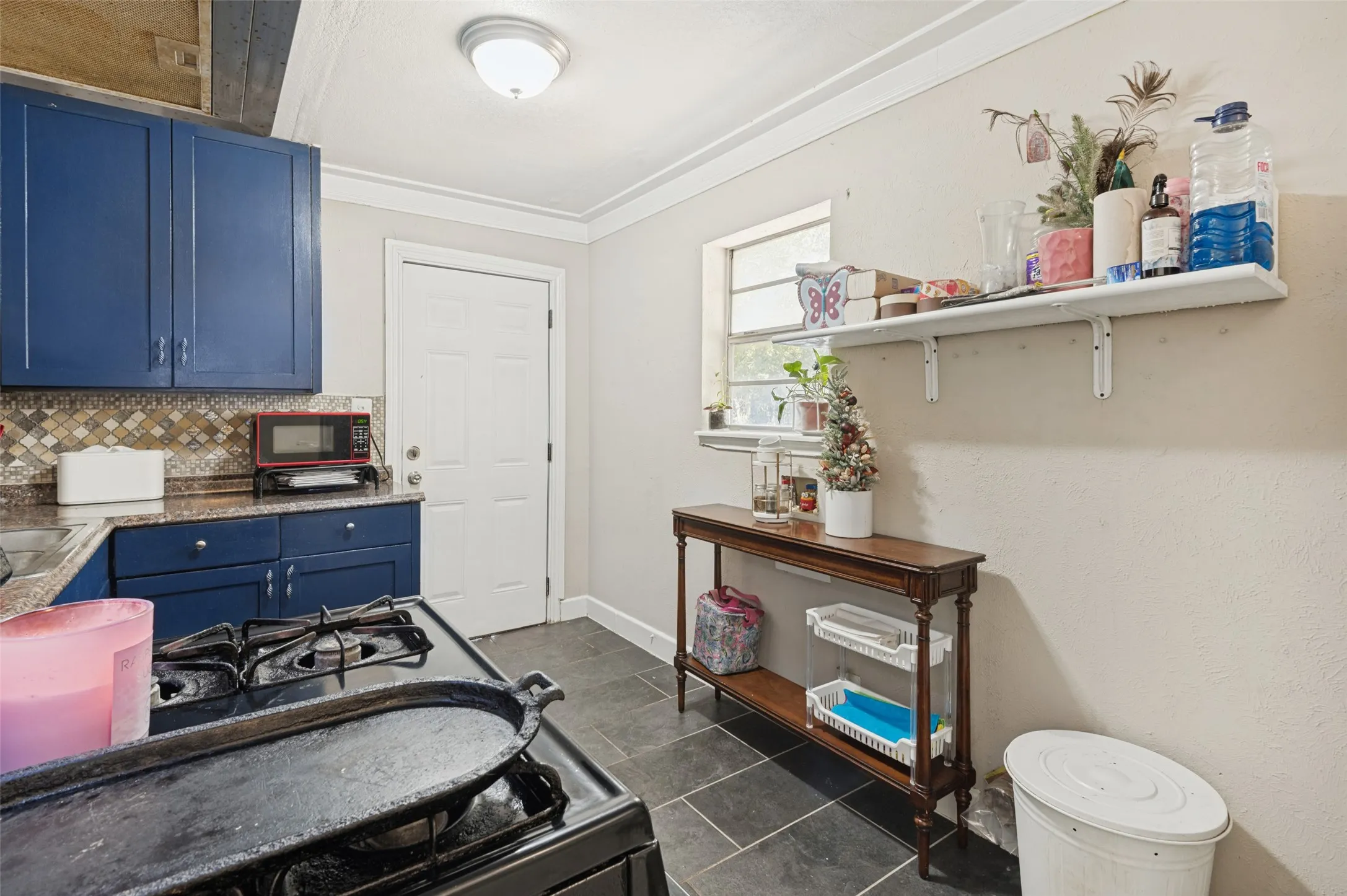 Blue cabinetry with contrasting countertops, a tiled backsplash, and dark slate flooring