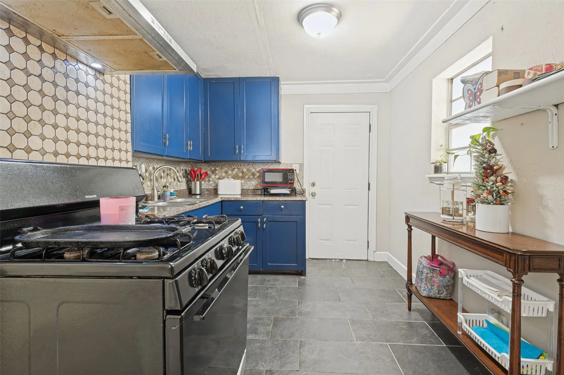 Kitchen featuring blue cabinetry, a tiled backsplash, dark countertops, and dark tile flooring