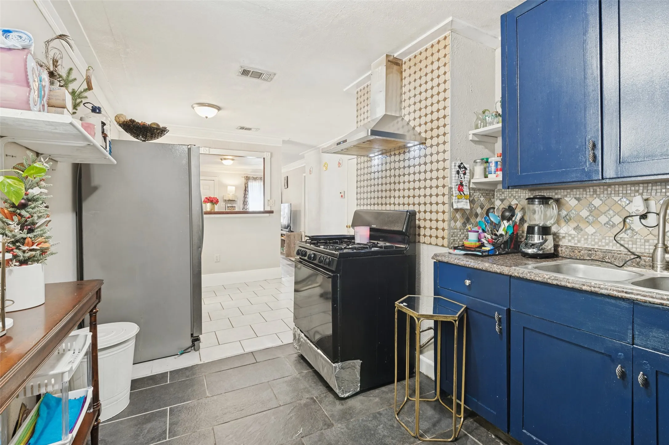 Kitchen featuring slate-look tile flooring, blue cabinetry, a stainless steel range hood, and a decorative tile backsplash