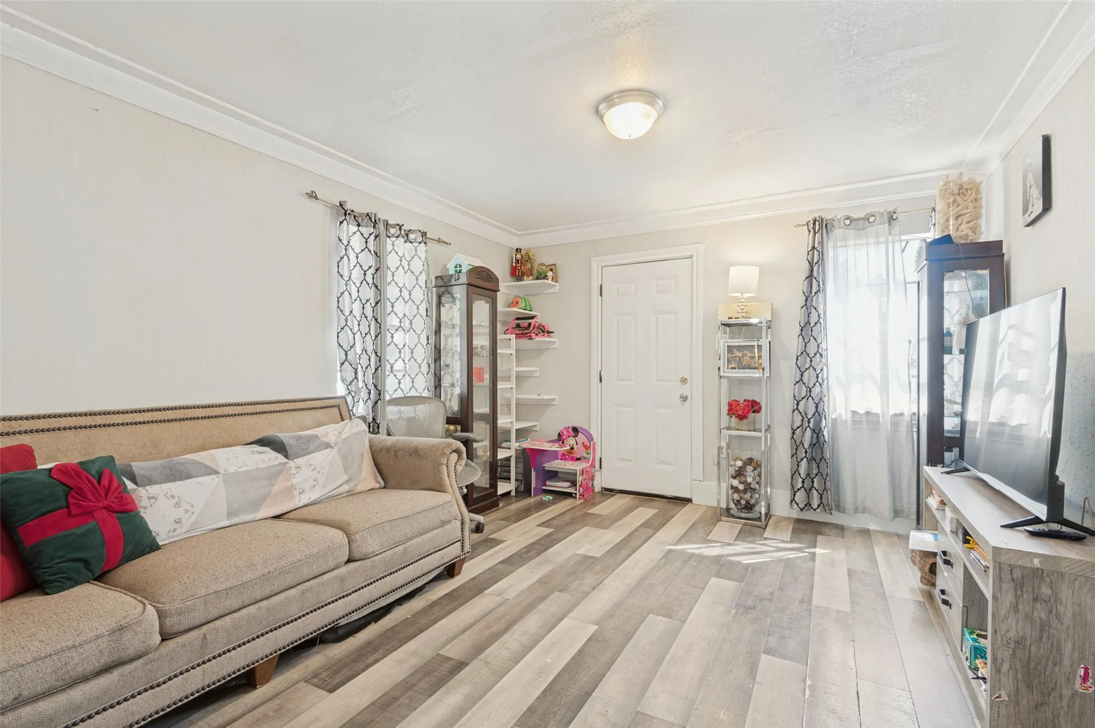 Wood-finish flooring, white paneled door, flush-mount ceiling light, and crown molding