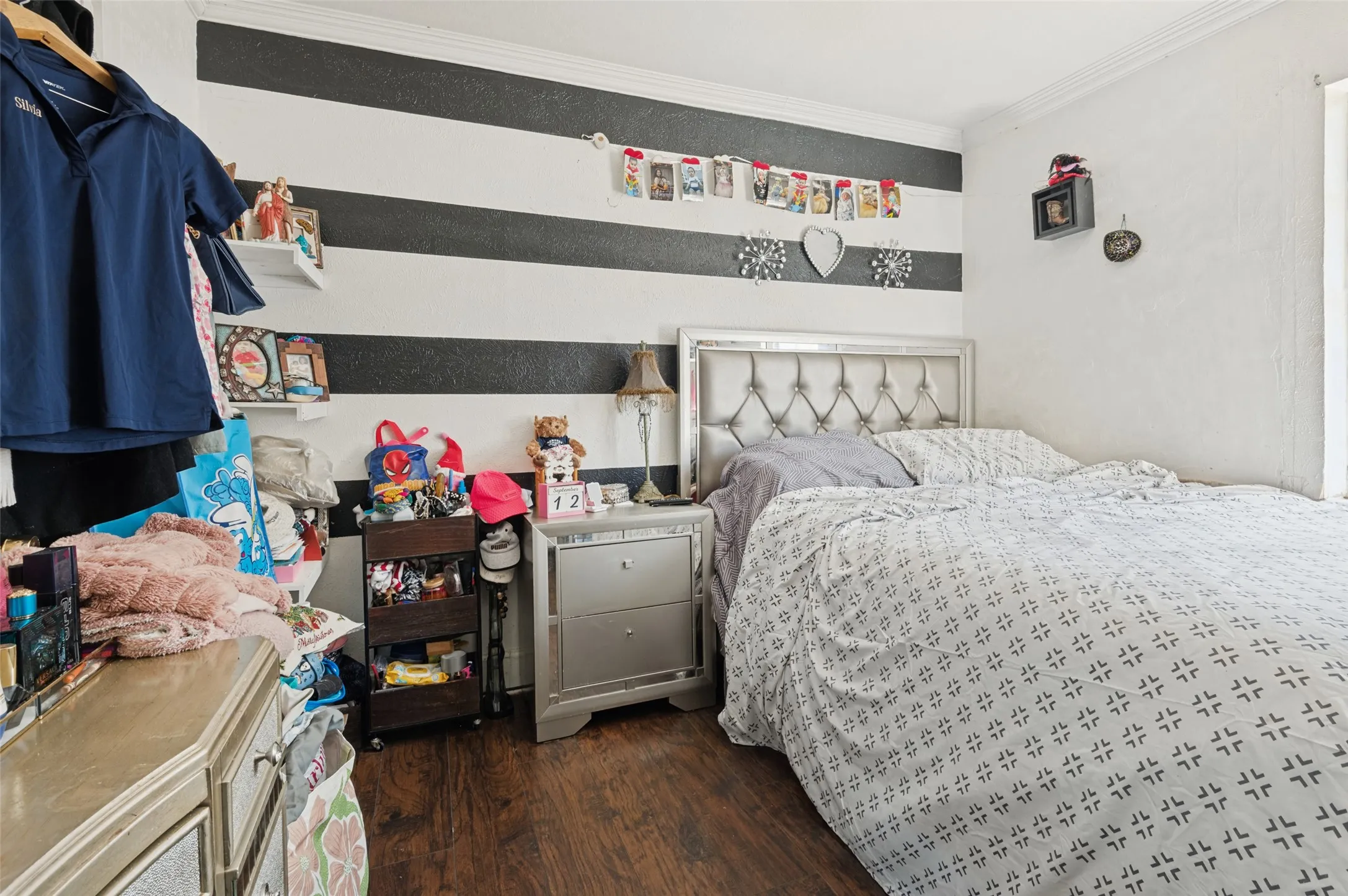 Wood-finish flooring with white and black striped accent wall, white crown molding, and white walls