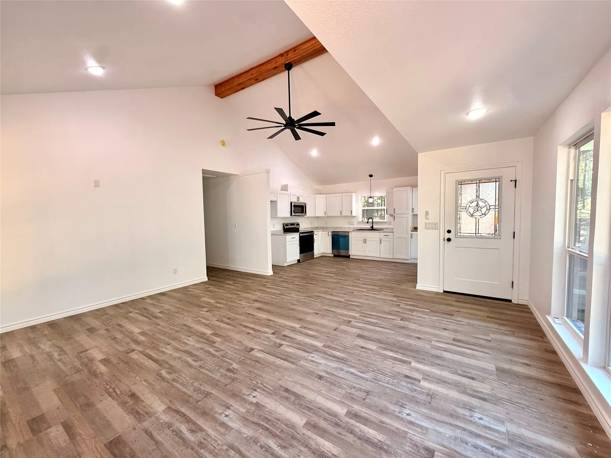 Vaulted ceiling with an exposed wood beam, wood-finish flooring, recessed lighting, and a white entry door with decorative glass