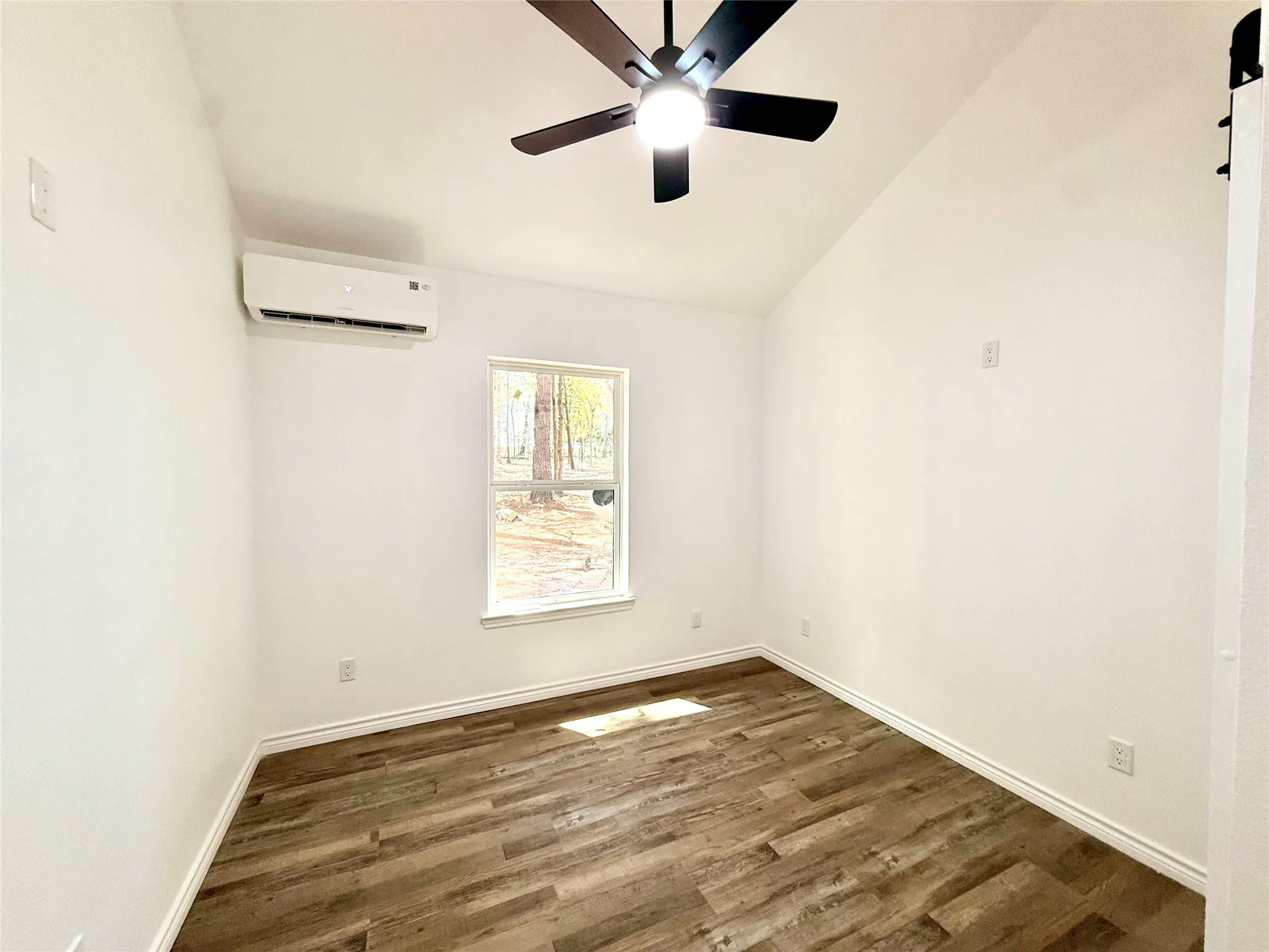 Vaulted ceiling with a ceiling fan, wood-finish flooring, and a wall-mounted HVAC unit