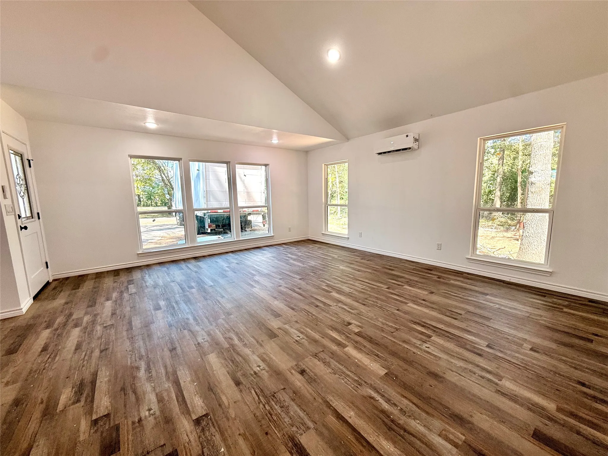 Vaulted ceiling, wood-finish flooring, recessed lighting, multiple windows, and a wall-mounted climate control unit