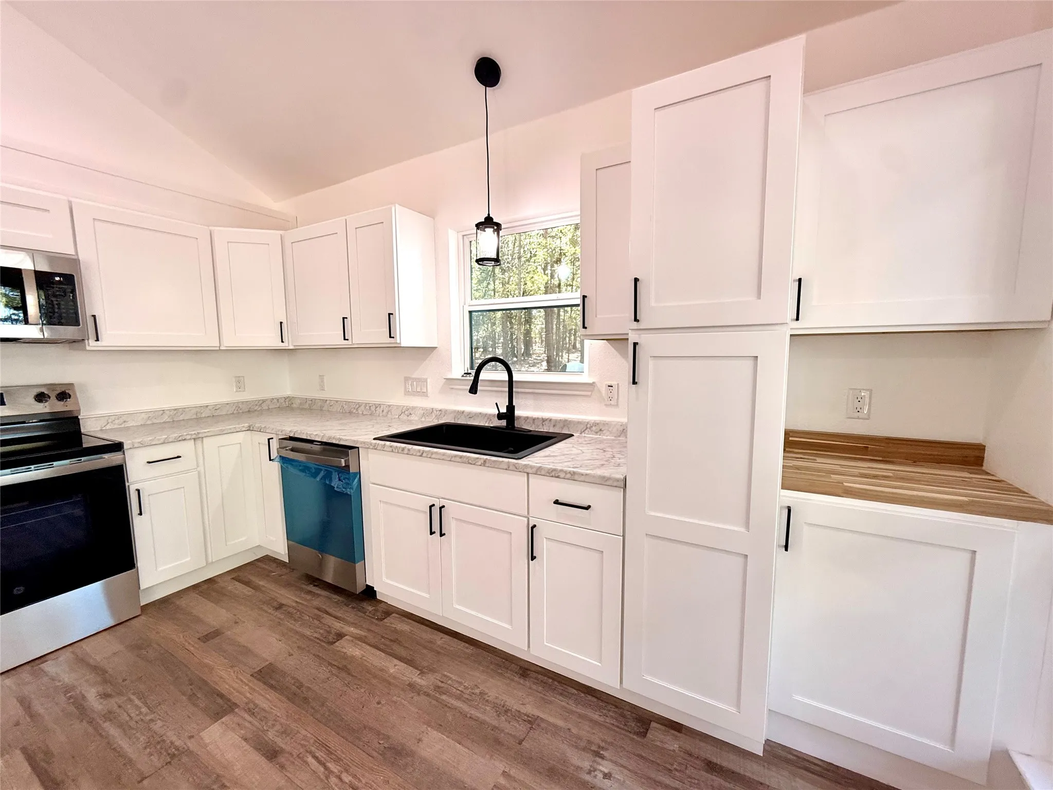 White shaker-style cabinetry with black hardware, wood-finish flooring, light-colored countertops, and stainless steel appliances