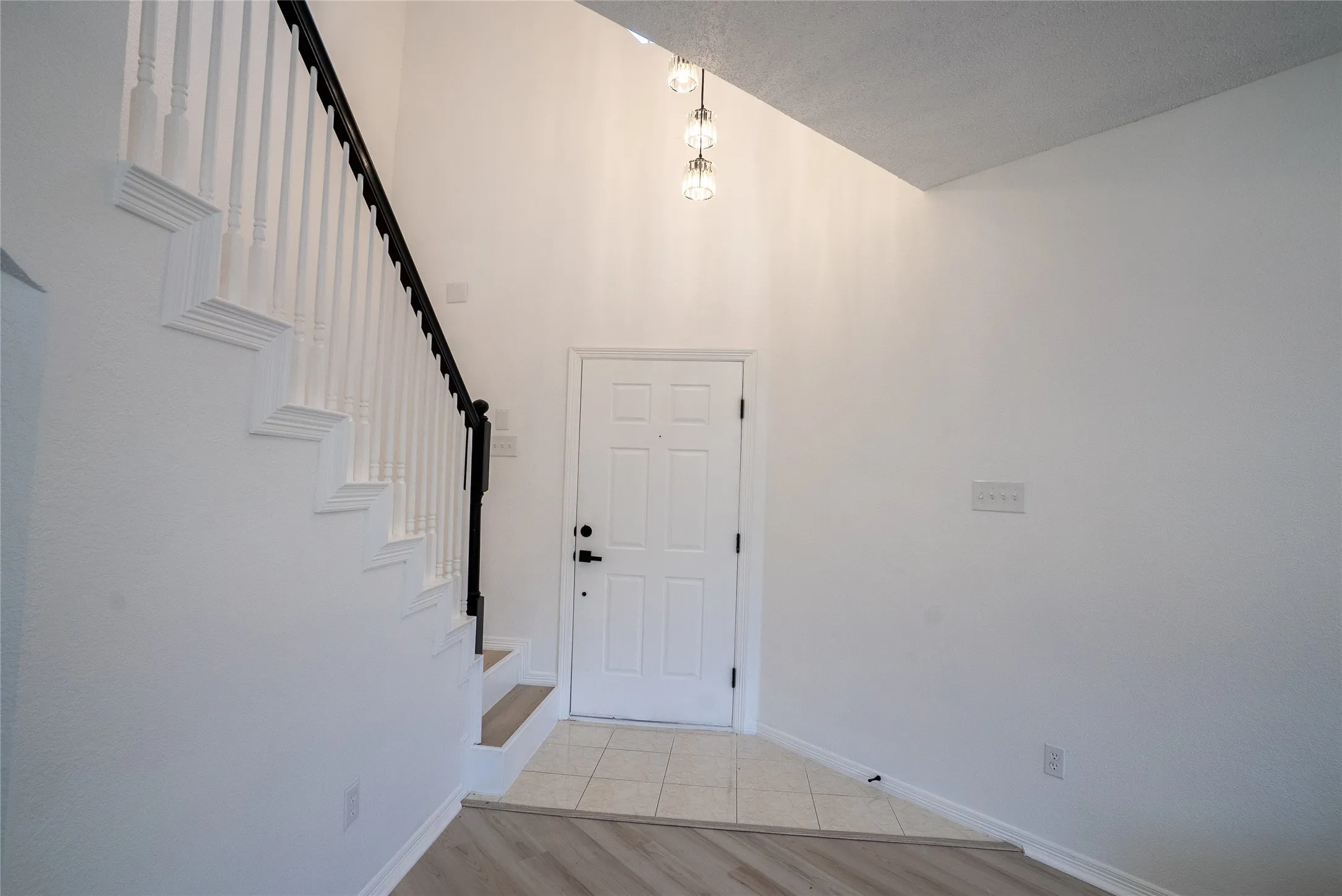 Entryway featuring a two-story ceiling, a staircase with white balusters and a dark handrail, a paneled door, and mixed flooring with tile and wood-finish planks