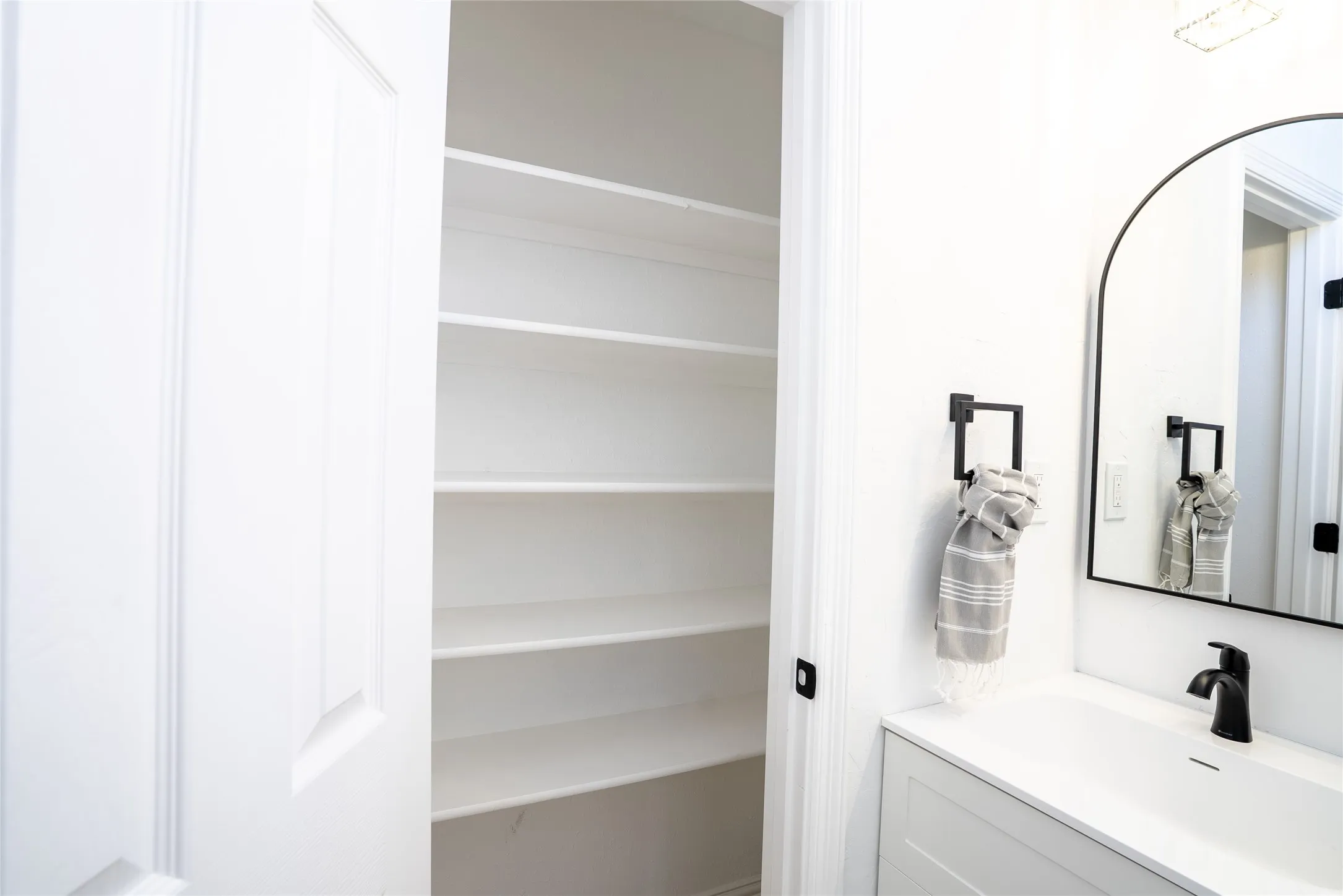 Built-in shelving, arched mirror, matte black faucet, and white vanity with integrated sink